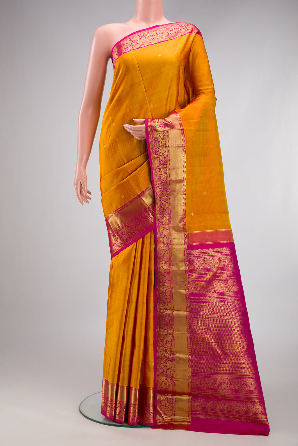 Mustard Kanjivaram Silk Saree with Zari Butta on the body and Zari Border.  displayed on a mannequin