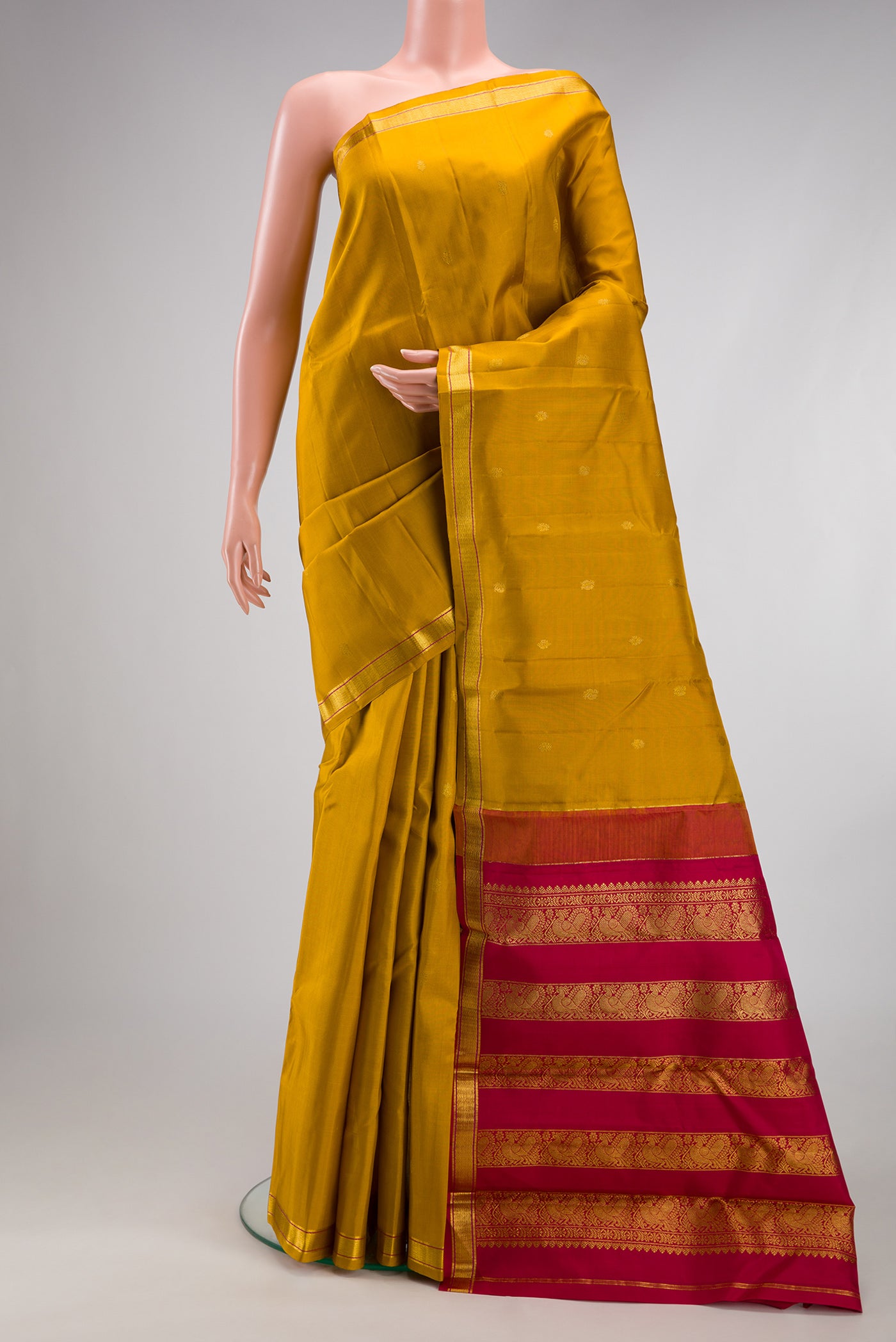 Mustard Kanchipuram Silk Saree with Zari Butta on the body and Zari Border.  displayed on a mannequin