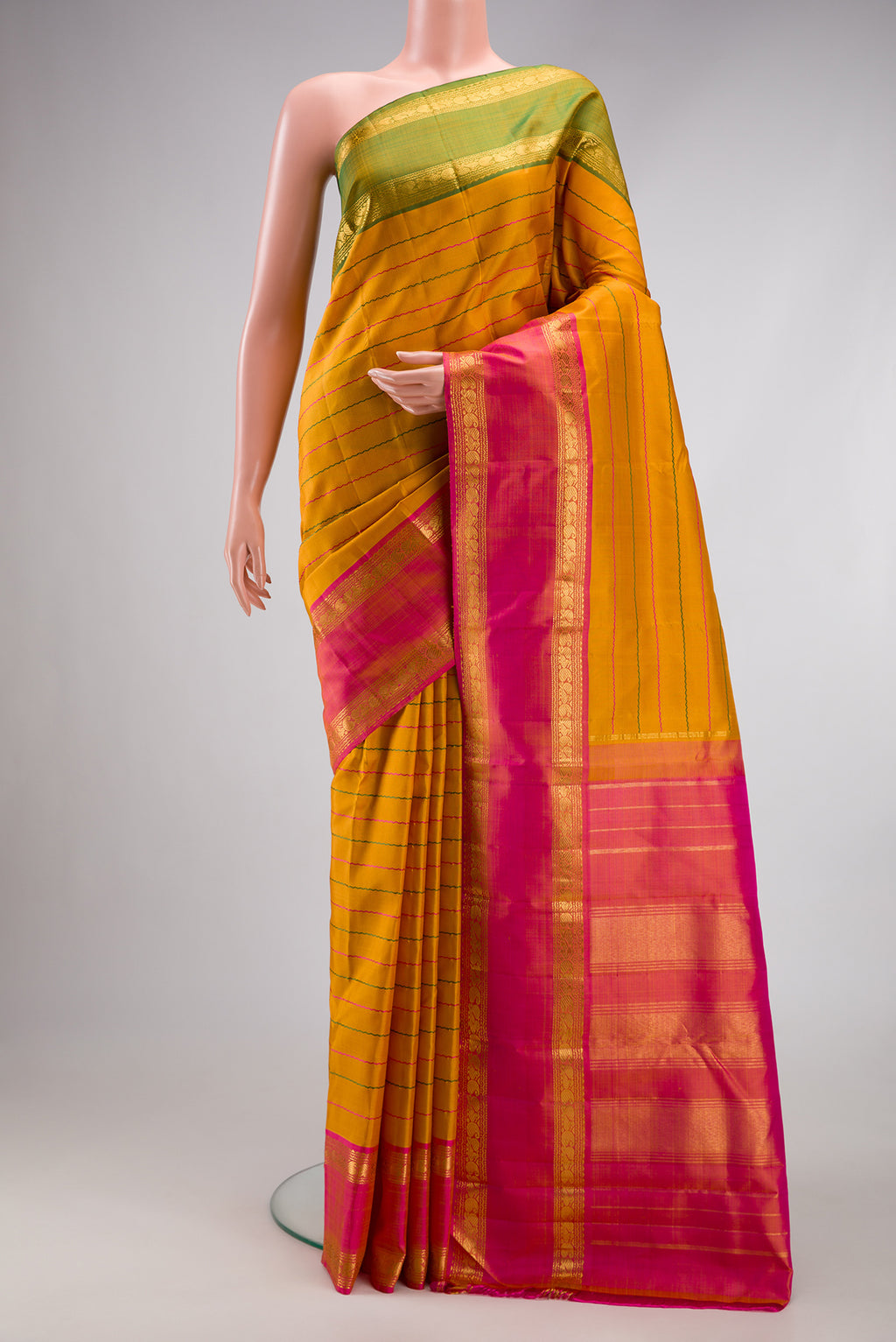 Mustard Kanchipuram Silk Saree with Veldhari on the body and Ganga Jamuna Border.  displayed on a mannequin