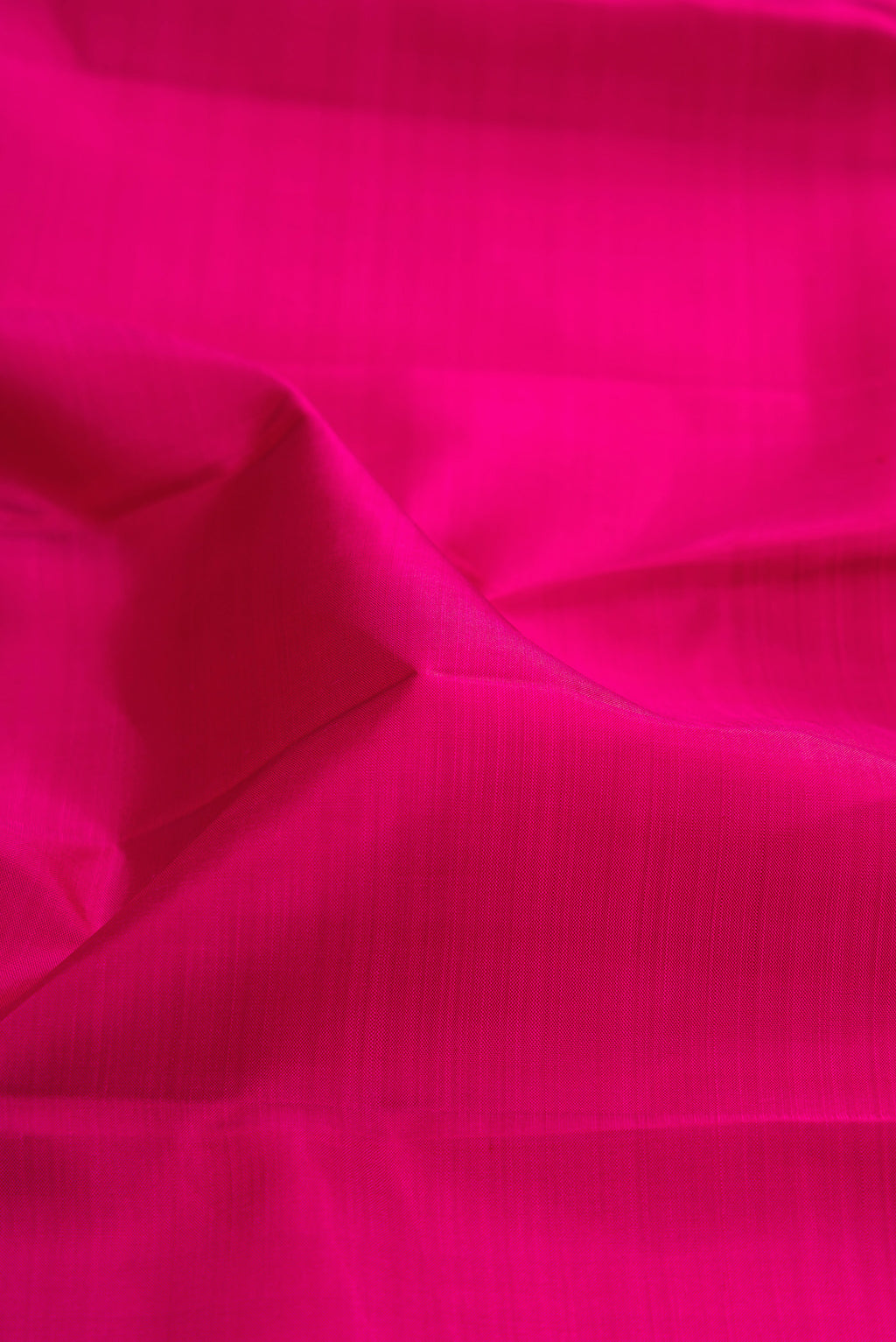 Close up of Rani Pink Kanjivaram Silk Saree with Plain Body and Zari Border.  displaying folds