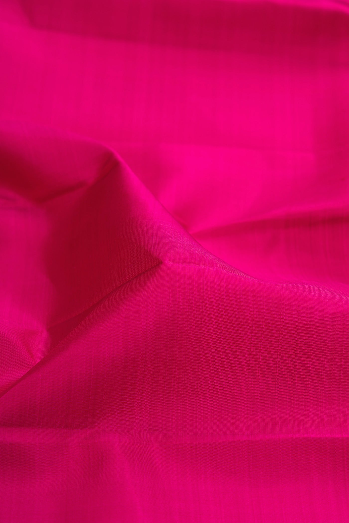 Close up of Rani Pink Kanjivaram Silk Saree with Plain Body and Zari Border.  displaying folds