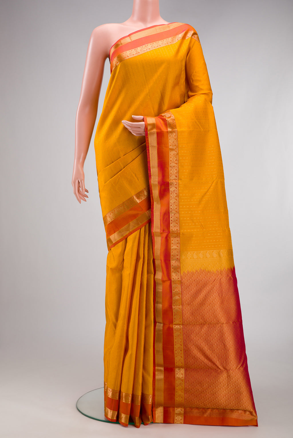 Mustard Kanchipuram Silk Saree with Zari Butta on the body and Zari Border.  displayed on a mannequin