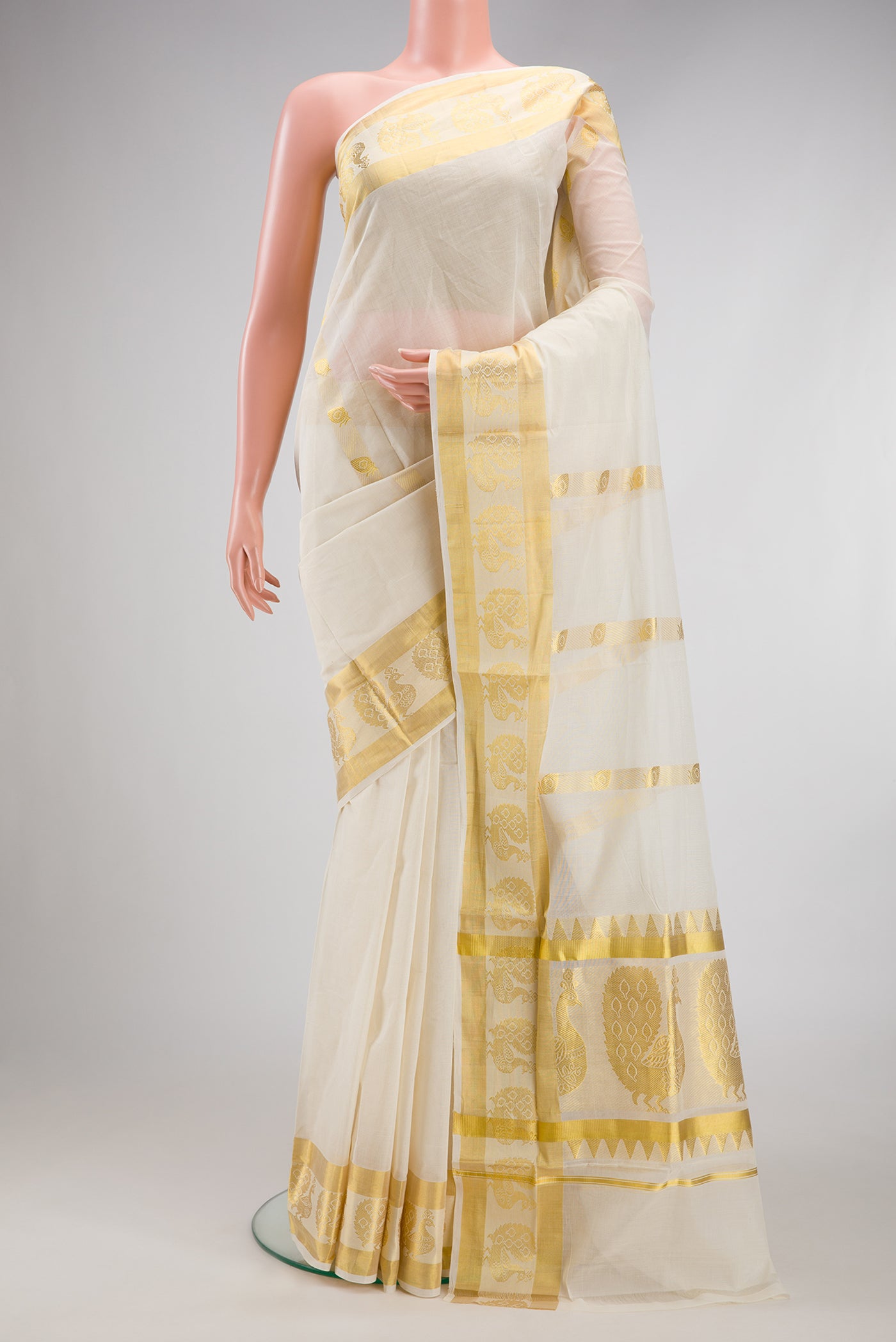 Off White Kerala Cotton Saree with Zari Butta on the body and Fancy Border.  displayed on a mannequin