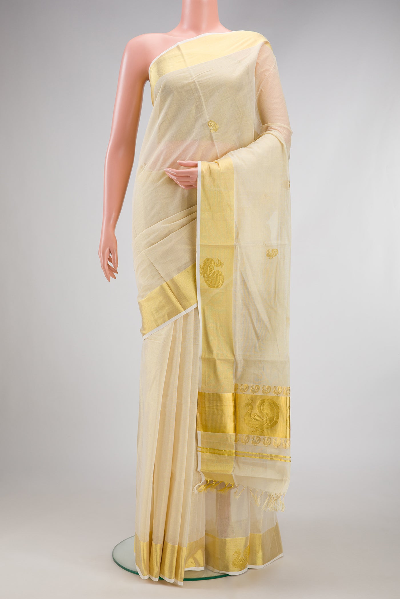 Gold Kerala Cotton Saree with Zari Butta on the body and Zari Border.  displayed on a mannequin