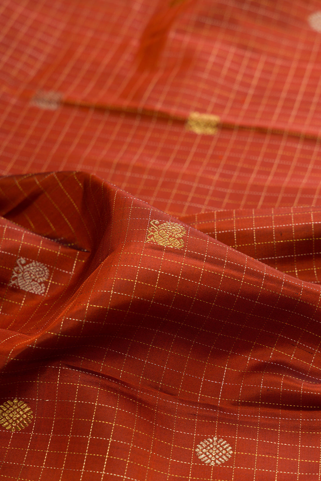Close up of Pure Silk Rust Kanchipuram Saree with Checked design on the body and Zari Border.  displaying folds