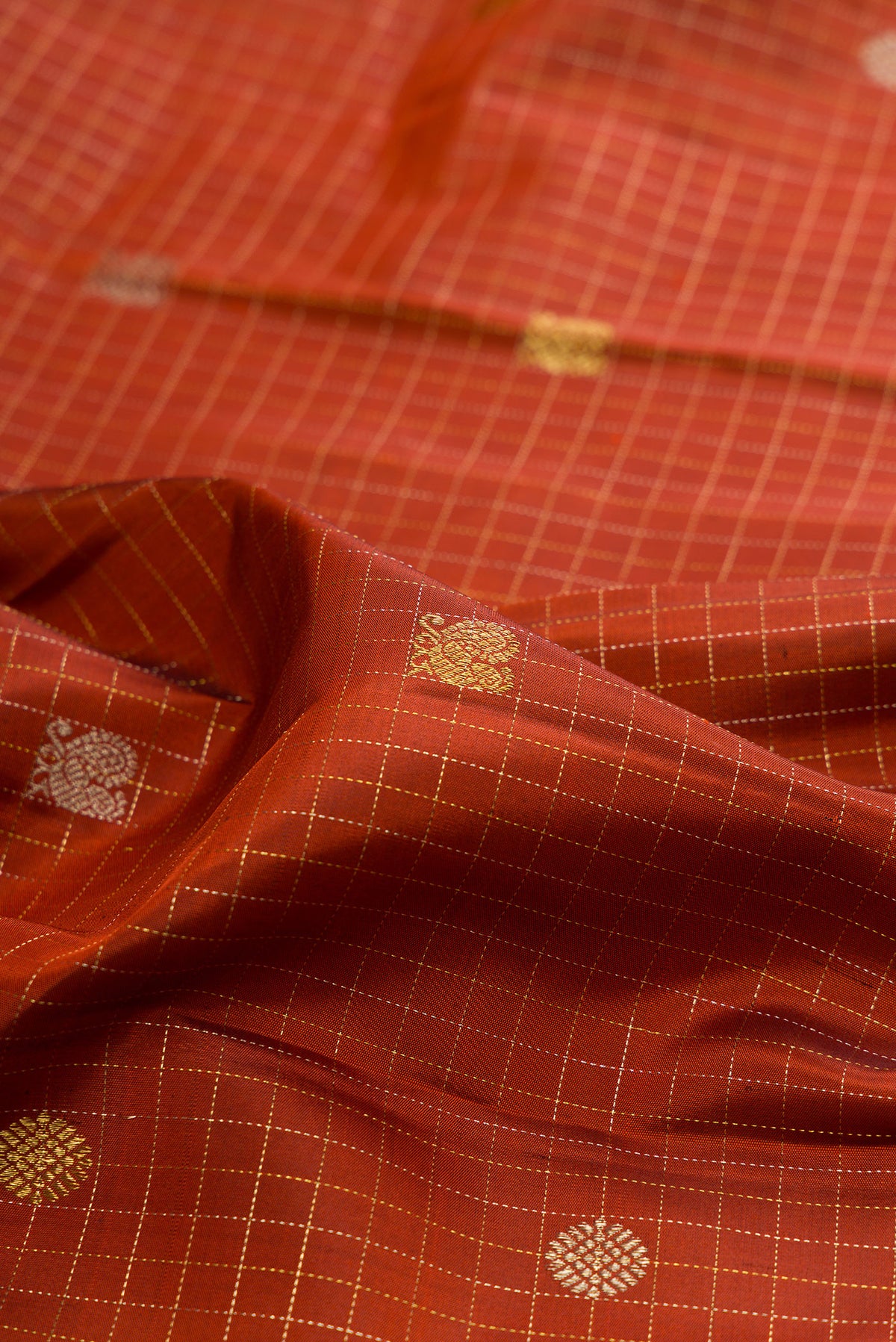 Close up of Pure Silk Rust Kanchipuram Saree with Checked design on the body and Zari Border.  displaying folds