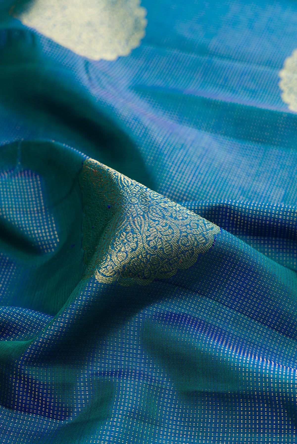 Close up of Pure Silk Peacock Blue Dual Tone Kanchipuram Saree with Zari Butta on the body and Zari Border.  displaying folds