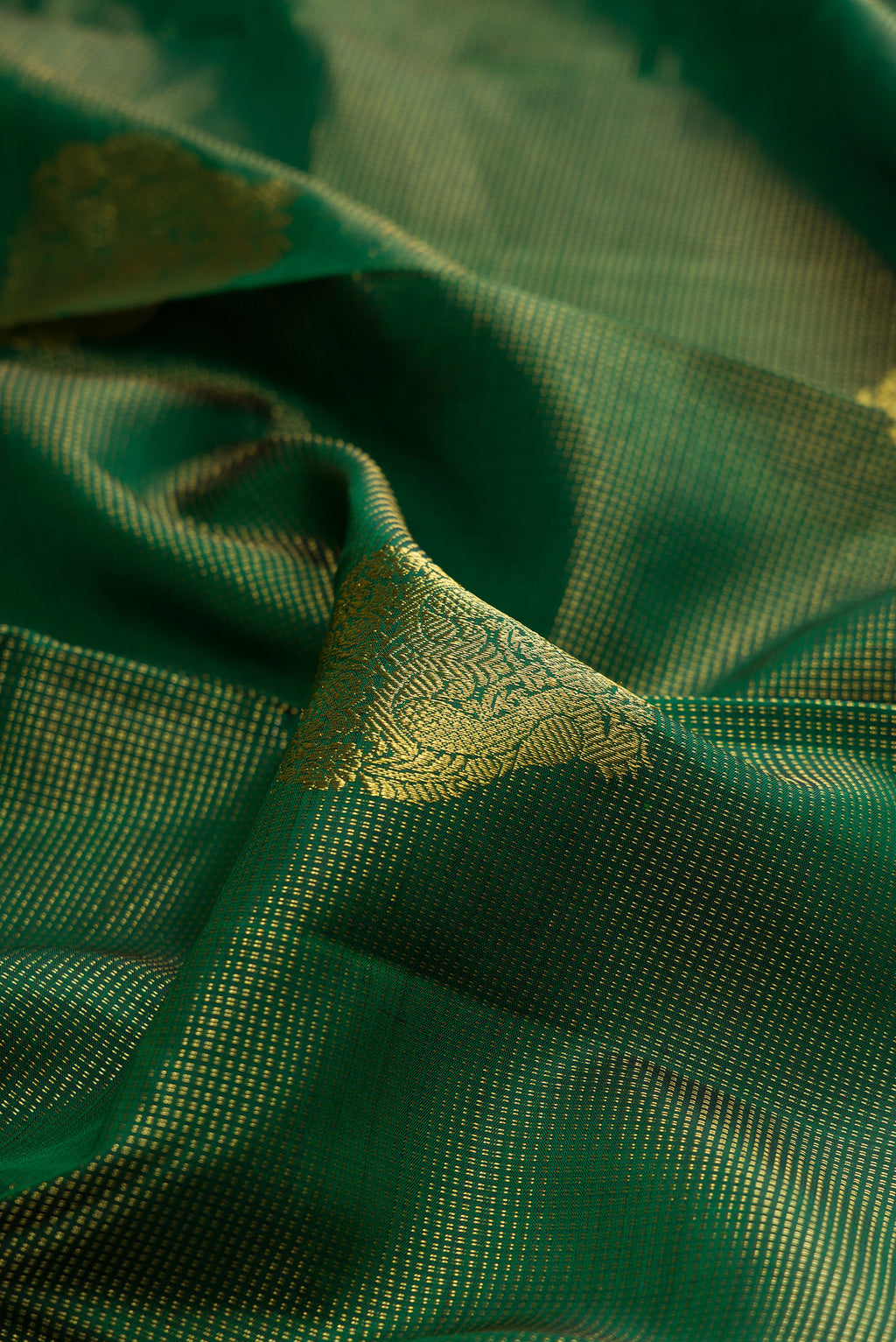 Close up of Pure Silk Bottle Green Kanchipuram Saree with Zari Butta on the body and Zari Border.  displaying folds
