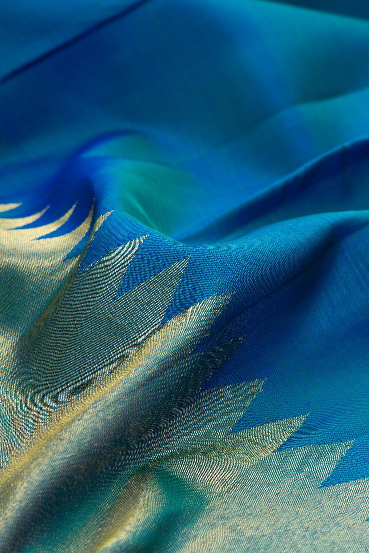 Close up of Pure Silk Peacock Blue Dual Tone Kanjivaram Saree with Plain Body and Rising Temple Border.  displaying folds