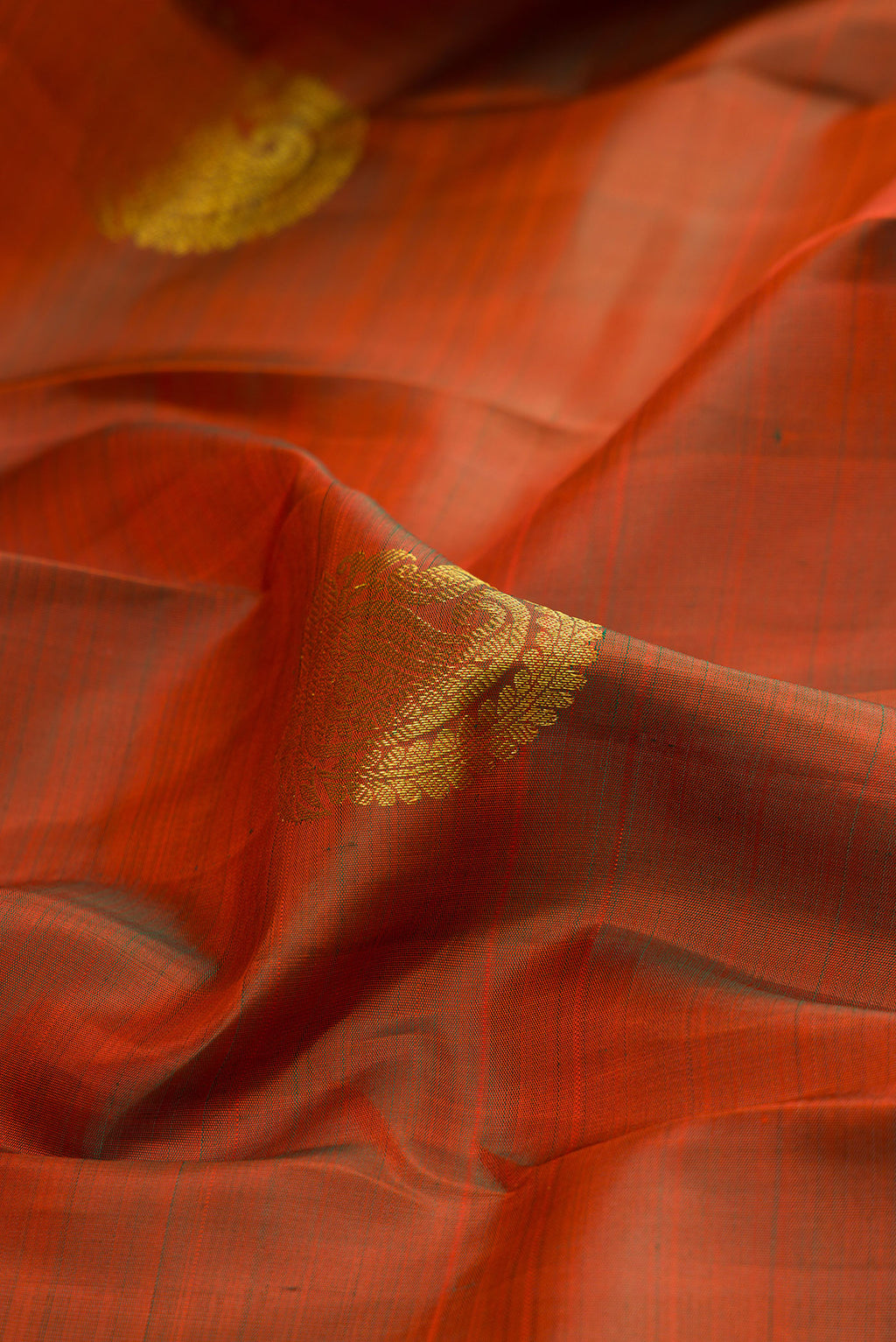 Close up of Pure Silk Rust Kanchipuram Saree with Zari Butta on the body and Zari Border.  displaying folds