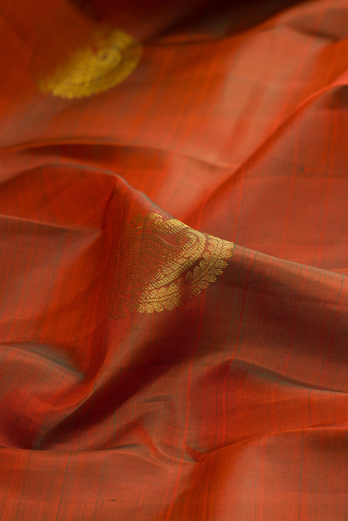 Close up of Pure Silk Rust Kanchipuram Saree with Zari Butta on the body and Zari Border.  displaying folds