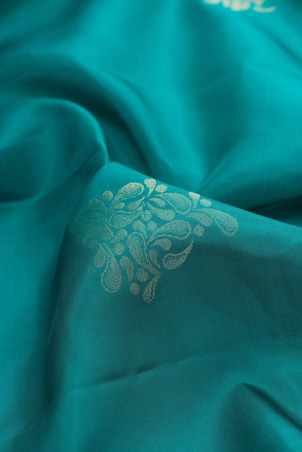 Close up of Pure Silk Teal Soft Saree with Zari Butta on the body and Zari Border.  displaying folds