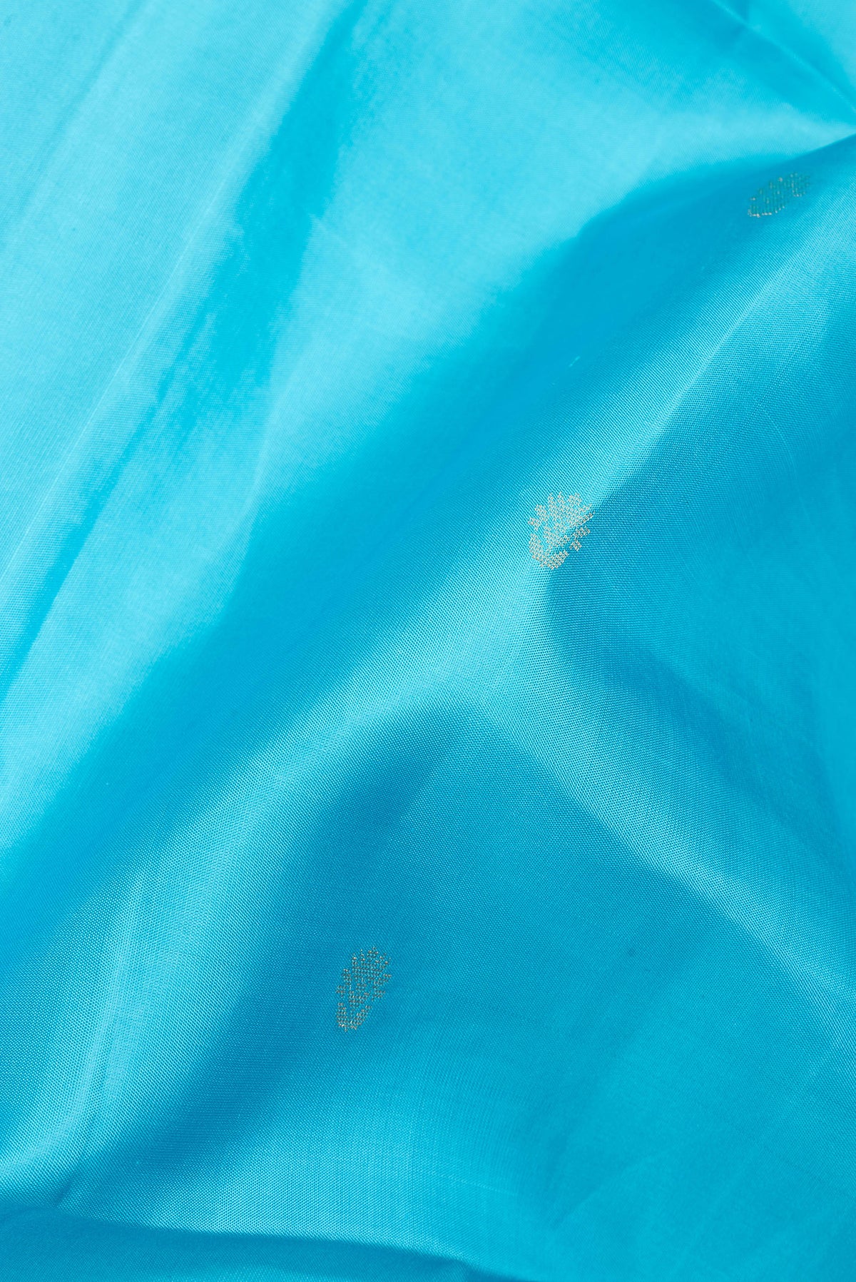 Close up of Pure Silk Sky Blue Soft Saree with Zari Butta on the body and Zari Border.  displaying folds