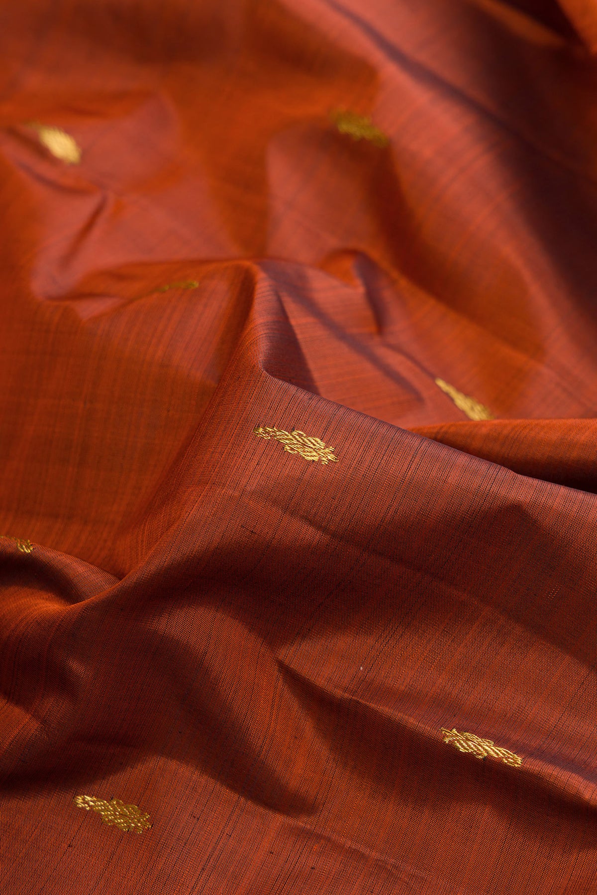 Close up of Pure Silk Rust Kanchipuram Saree with Zari Butta on the body and Zari Border.  displaying folds