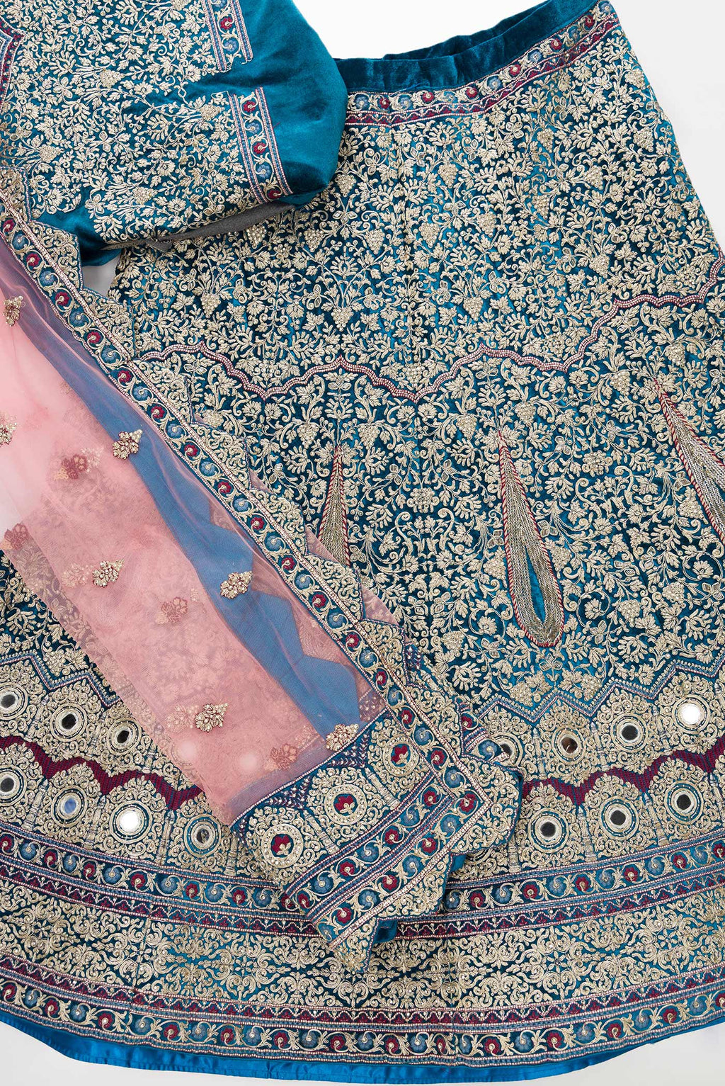 Flat lay of Peacock Blue Banarasi Silk Womens Lehenga set featuring Embroidered Choli paired with Peacock Blue Embroidered Skirt with Embroidered Border and a Embroidered dupatta in Pink