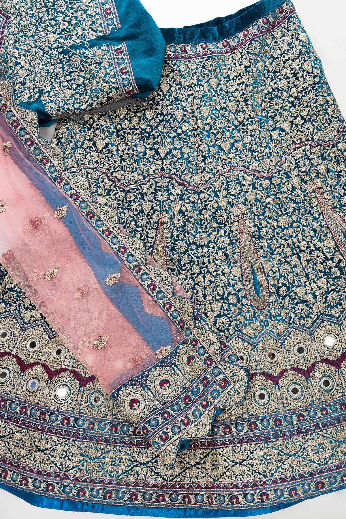 Flat lay of Peacock Blue Banarasi Silk Womens Lehenga set featuring Embroidered Choli paired with Peacock Blue Embroidered Skirt with Embroidered Border and a Embroidered dupatta in Pink