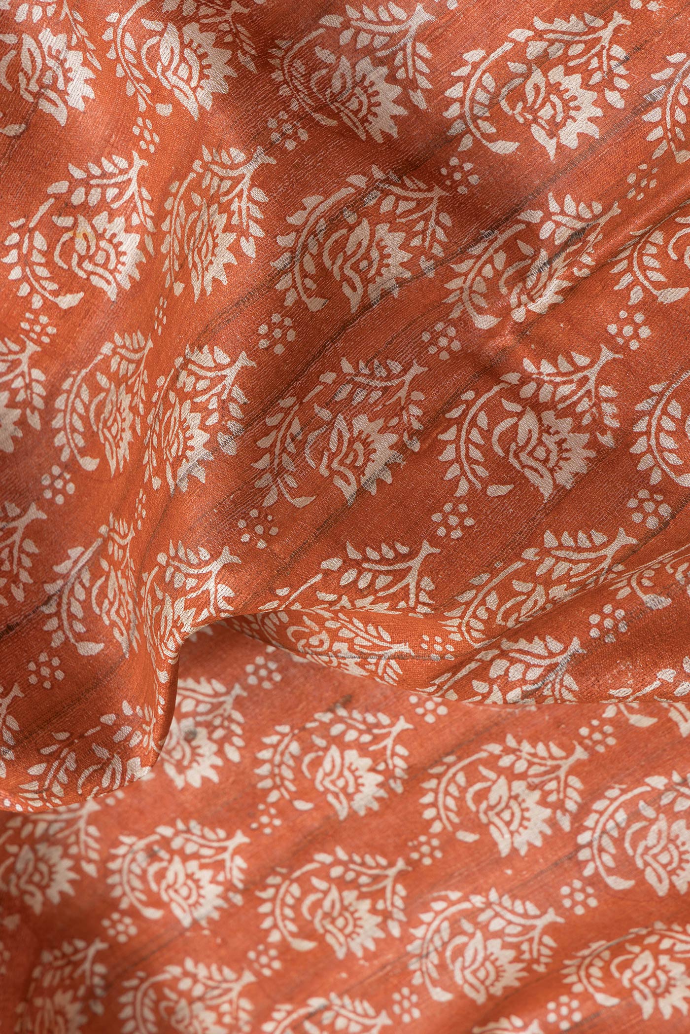 Close up of Orange Dual Tone Tussar Silk Saree with Printed design on the body and Printed Border.  displaying folds