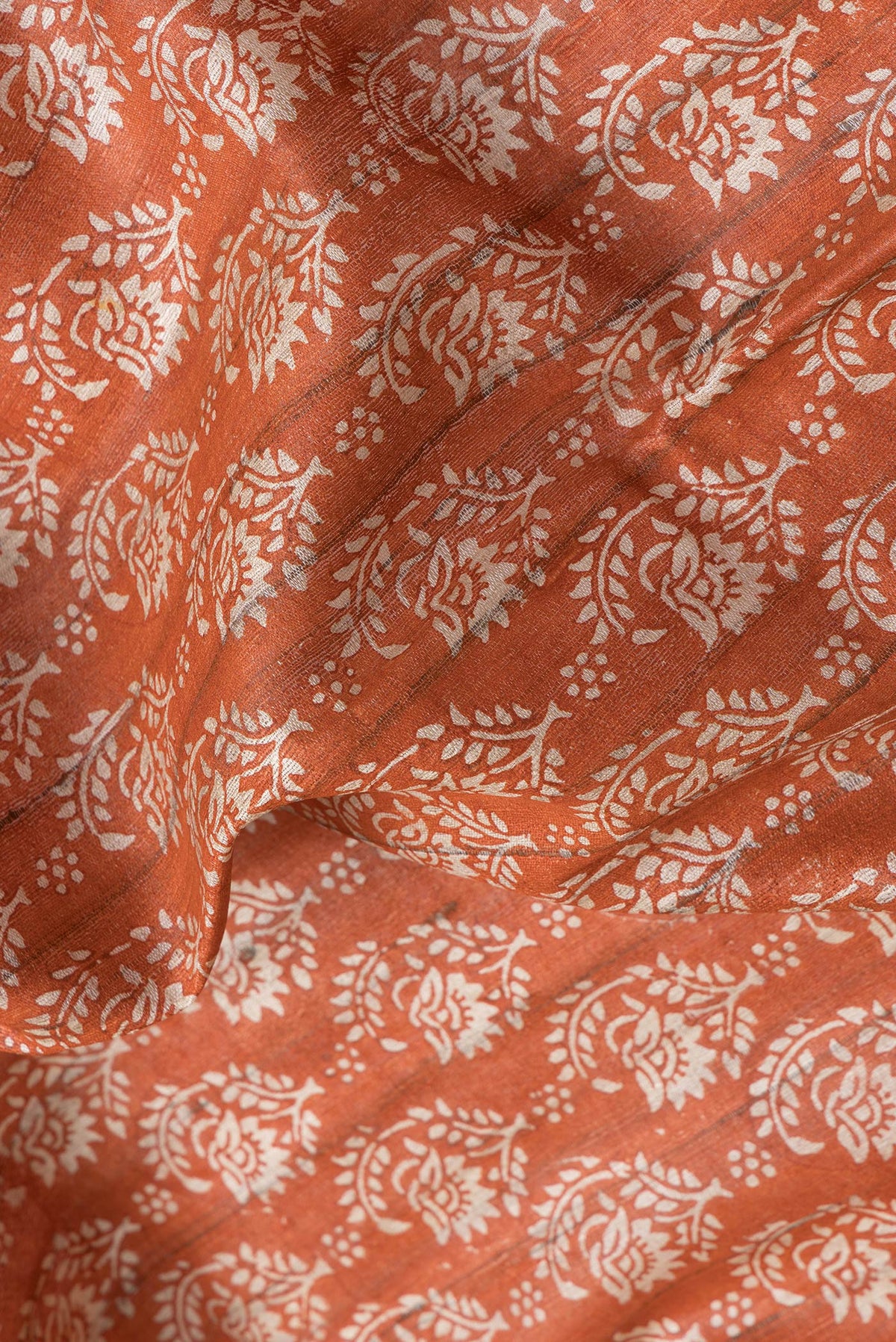 Close up of Orange Dual Tone Tussar Silk Saree with Printed design on the body and Printed Border.  displaying folds