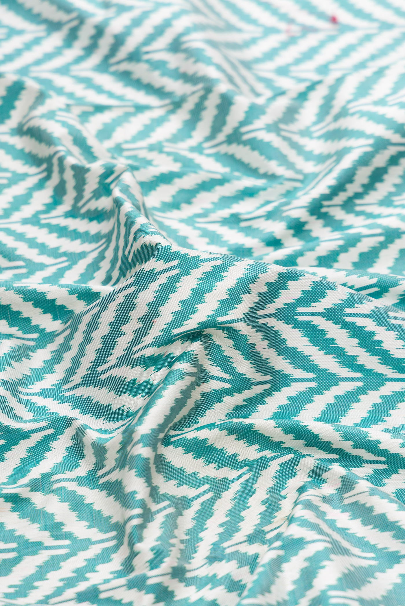 Close up of Off White and Green Color Double Ikat Saree with Ikat Print on the body and Ikat Border.  displaying folds