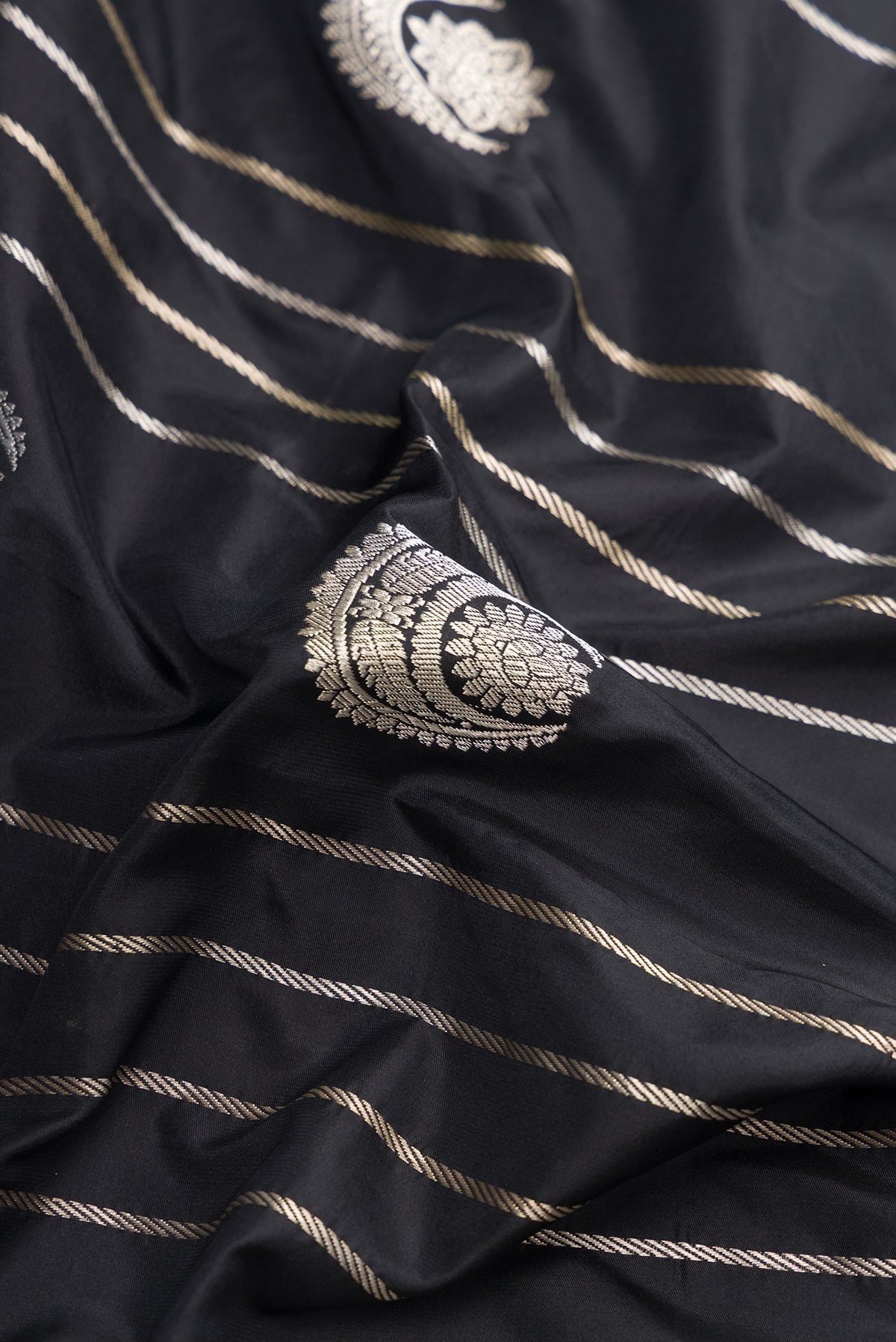 Close up of Black Dual Tone Banarasi Silk Saree with Zari Butta on the body and Zari Border.  displaying folds