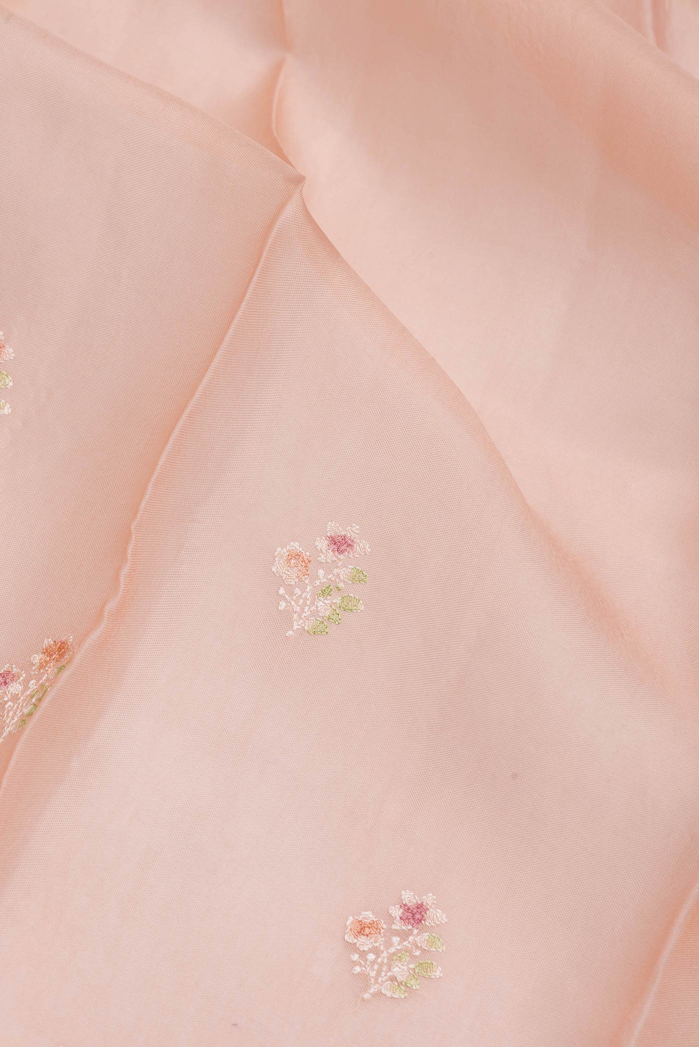 Close up of Peach Dual Tone Organza Silk Saree with Zari Butta on the body and Zari Border.  displaying folds