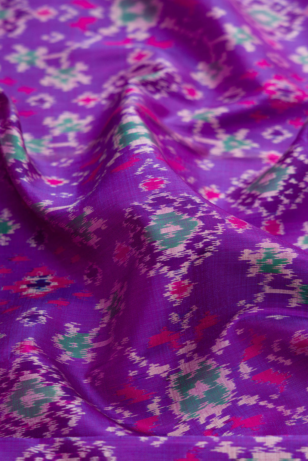 Close up of Purple Dual Tone Kanjivaram Silk Saree with Ikat Print on the body and Zari Border.  displaying folds