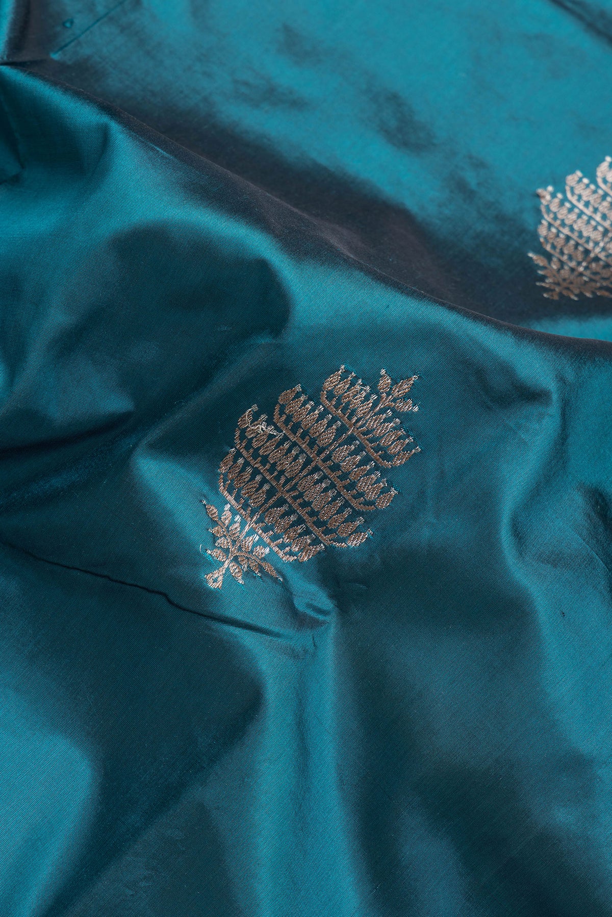 Close up of Peacock Blue Dual Tone Banarasi Silk Saree with Zari Butta on the body and Thread Border.  displaying folds