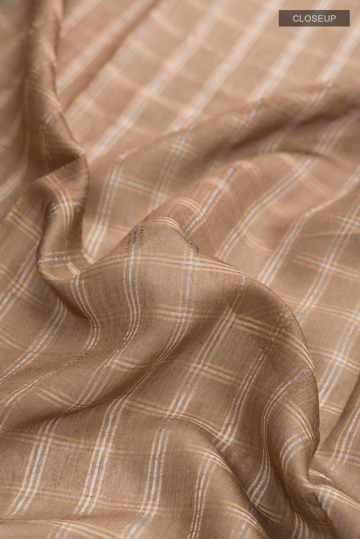 Close up of Beige Tussar Silk Saree with Checked design on the body and Zari Border displaying folds