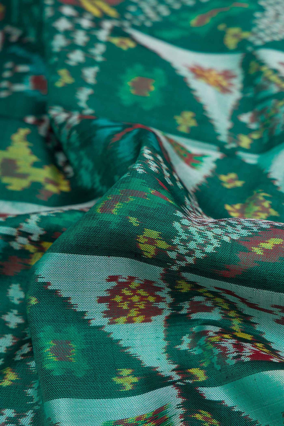 Close up of Green Dual Tone Rajkot Patola Silk Saree with Ikat Print on the body and Ikat Border displaying folds