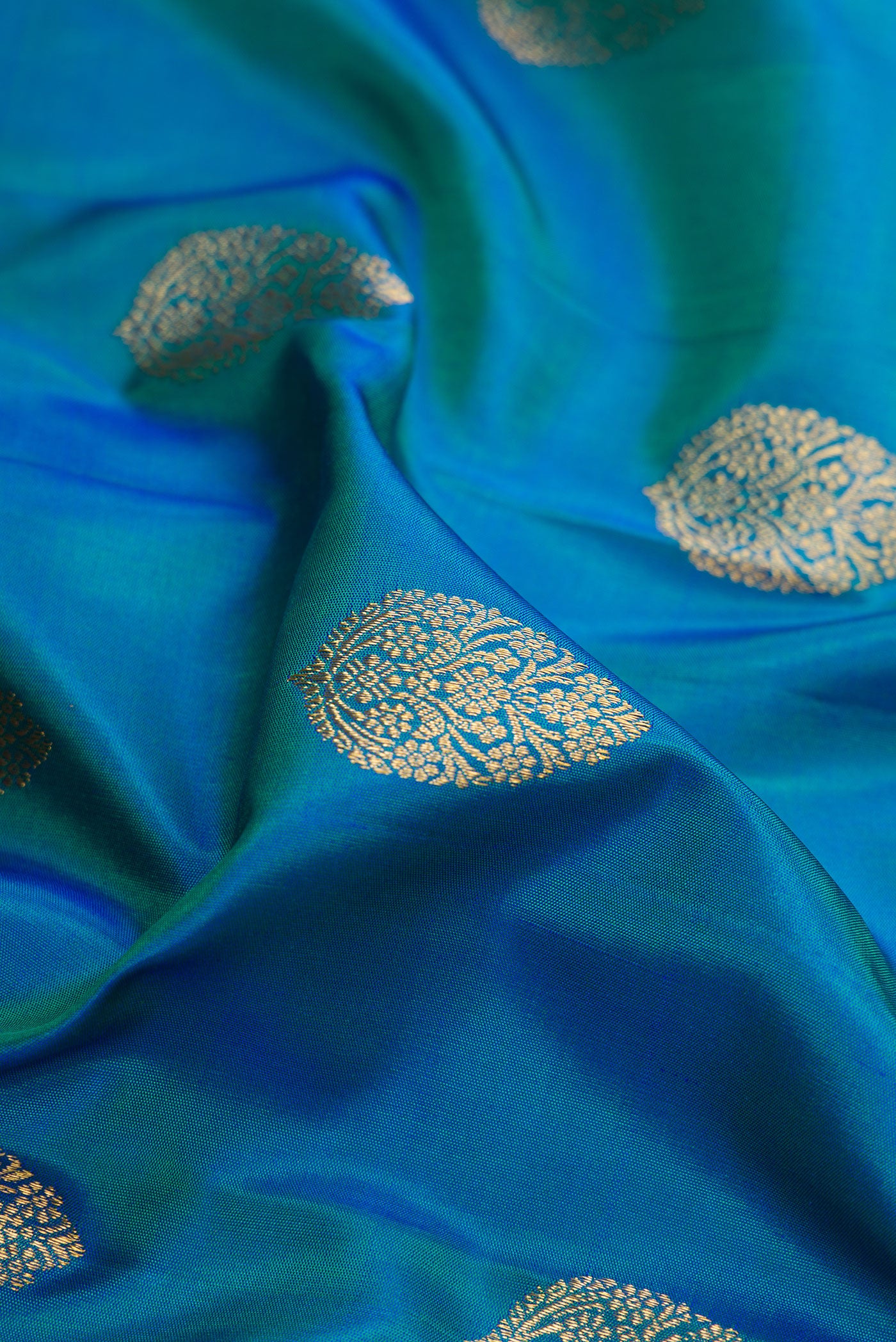 Close up of Pure Silk Pure Zari Peacock Blue Dual Tone Kanjivaram Saree with Zari Butta on the body and Zari Border.  displaying folds