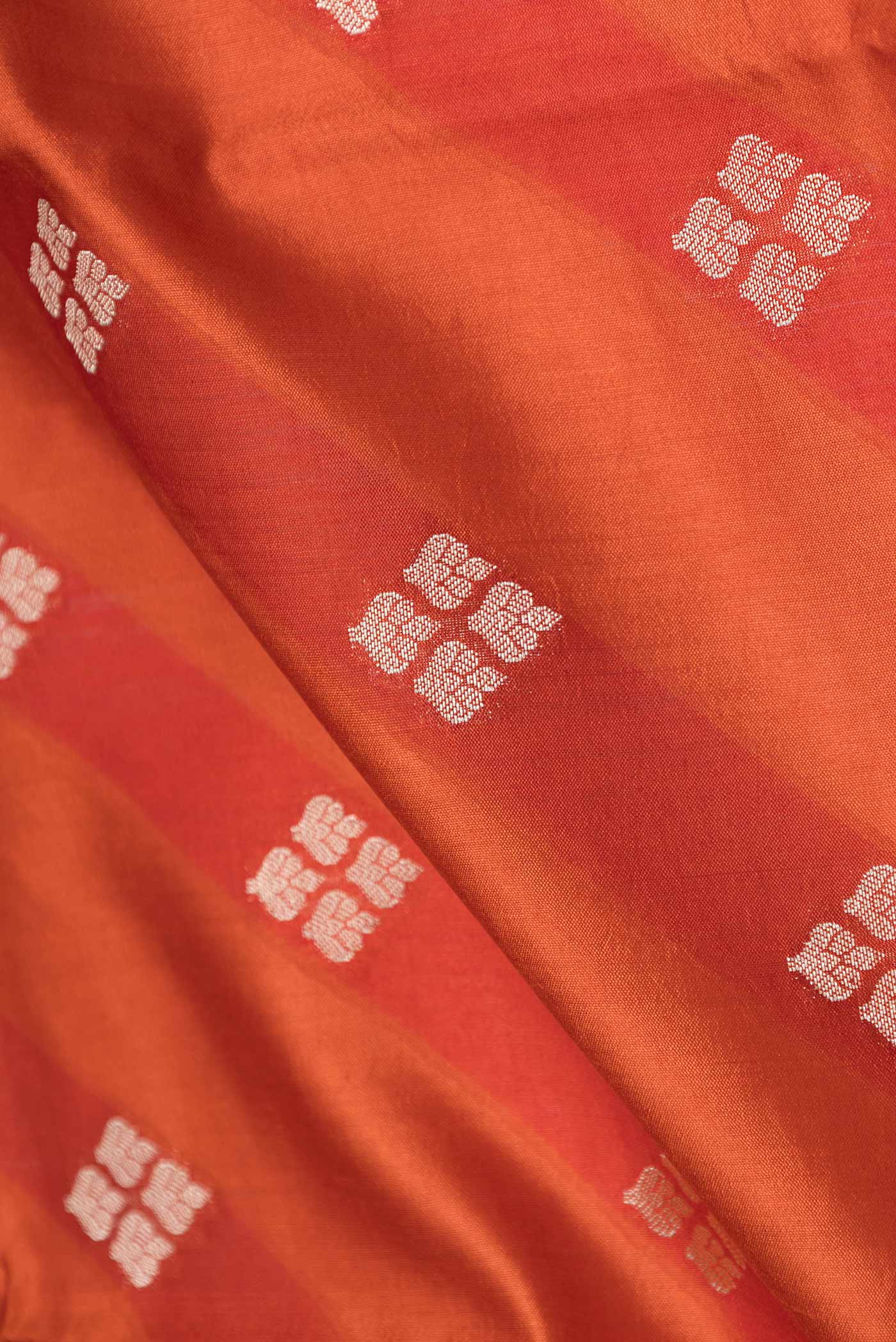 Close up of Orange Banarasi Raw Silk Saree with Zari Butta on the body and Zari Border displaying folds