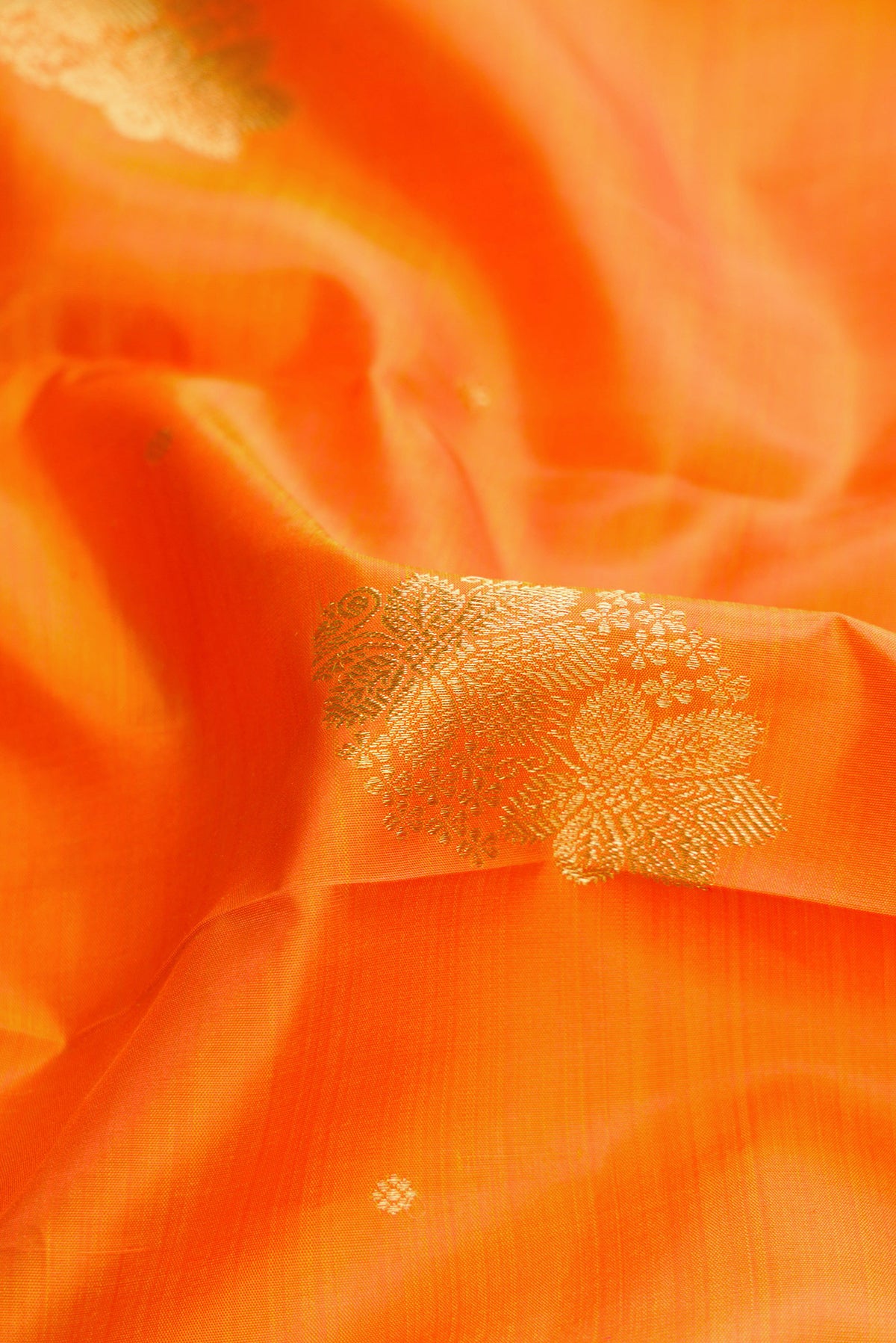 Close up of Orange Dual Tone Kanjivaram Silk Saree with Zari Butta on the body and Zari Border.  displaying folds
