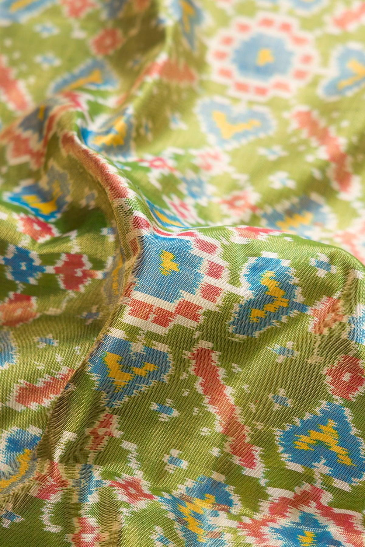 Close up of Pure Silk Pure Zari Mehandi Green Dual Tone Kanjivaram Tissue Saree with Ikat Print on the body and Zari Border.  displaying folds