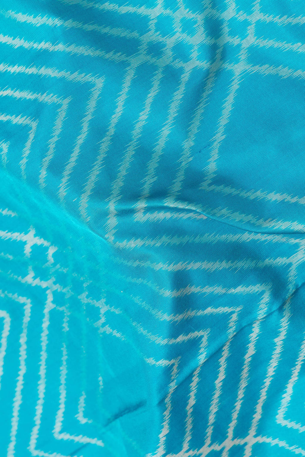 Close up of Sky Blue Dual Tone Double Ikat Saree with Ikat Print on the body and Plain Border.  displaying folds