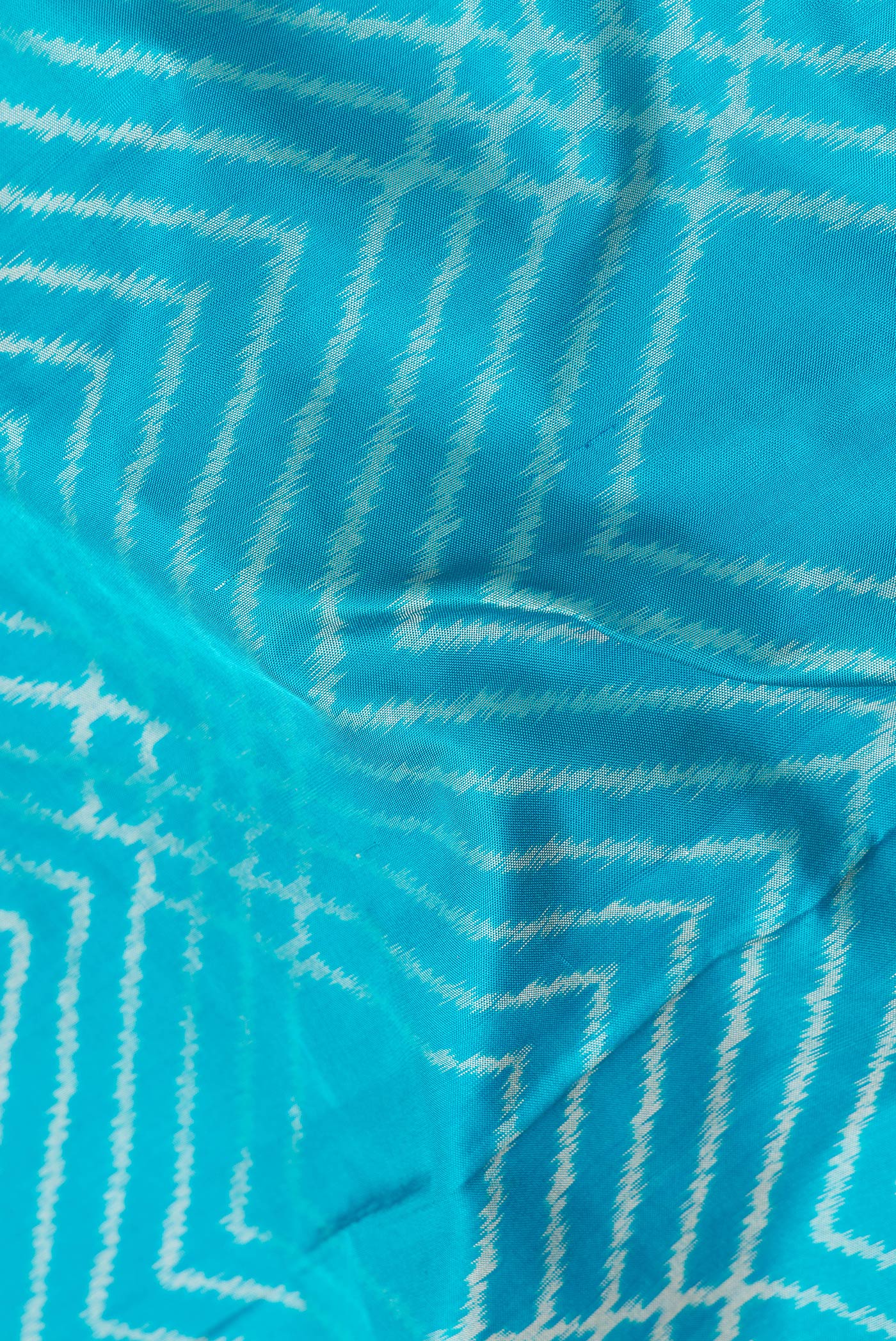 Close up of Sky Blue Dual Tone Double Ikat Saree with Ikat Print on the body and Plain Border.  displaying folds
