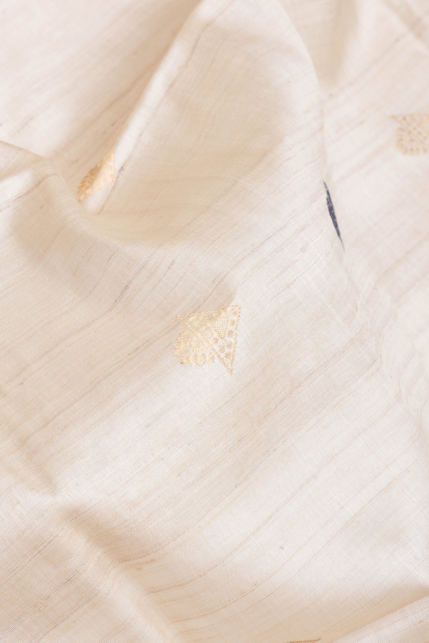 Close up of Beige Dual Tone Tussar Silk Saree with Zari And Thread Butta on the body and Zari Border.  displaying folds