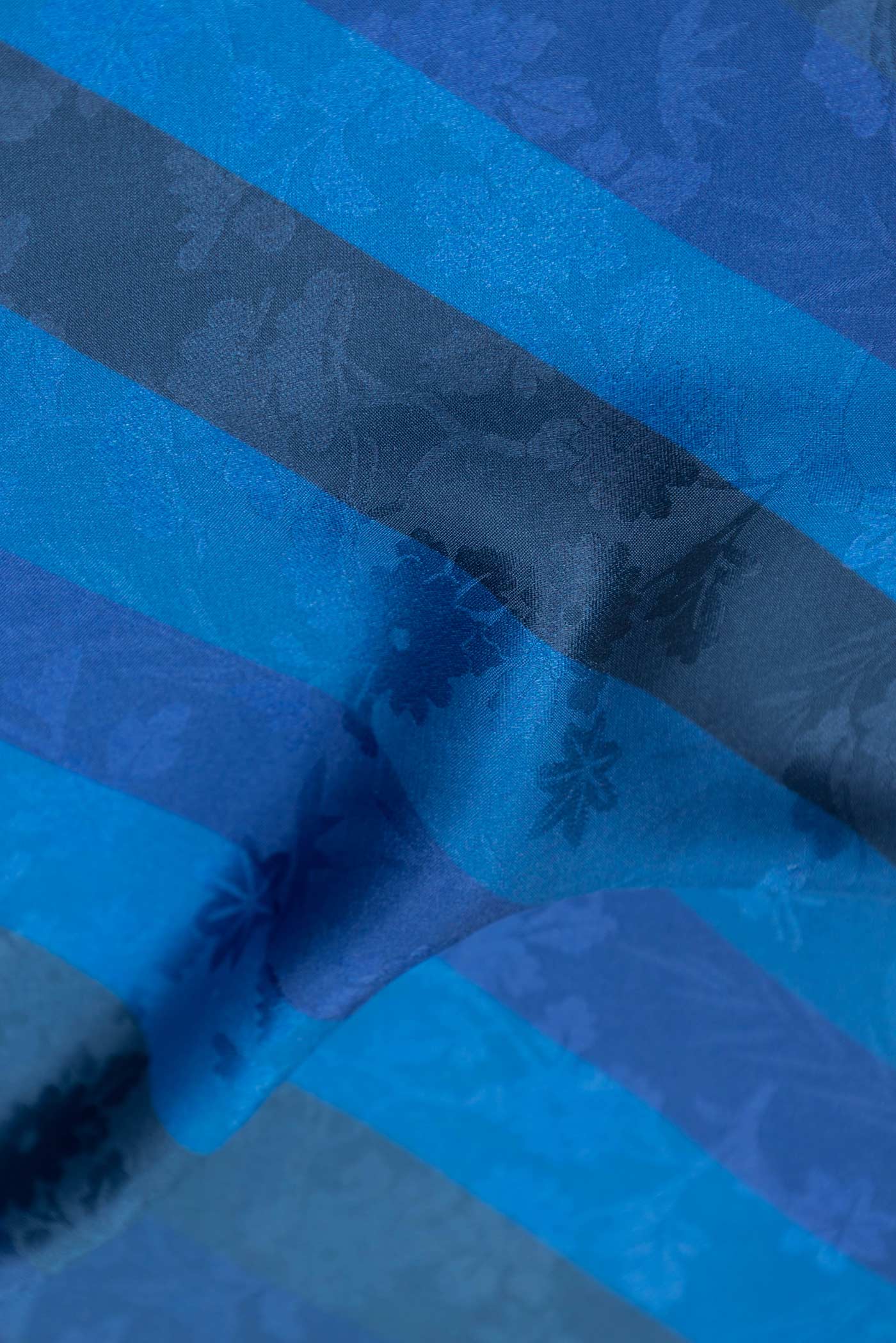 Close up of Blue Dual Tone Mysore Crepe Saree with Printed design on the body and Embroidery Border displaying folds