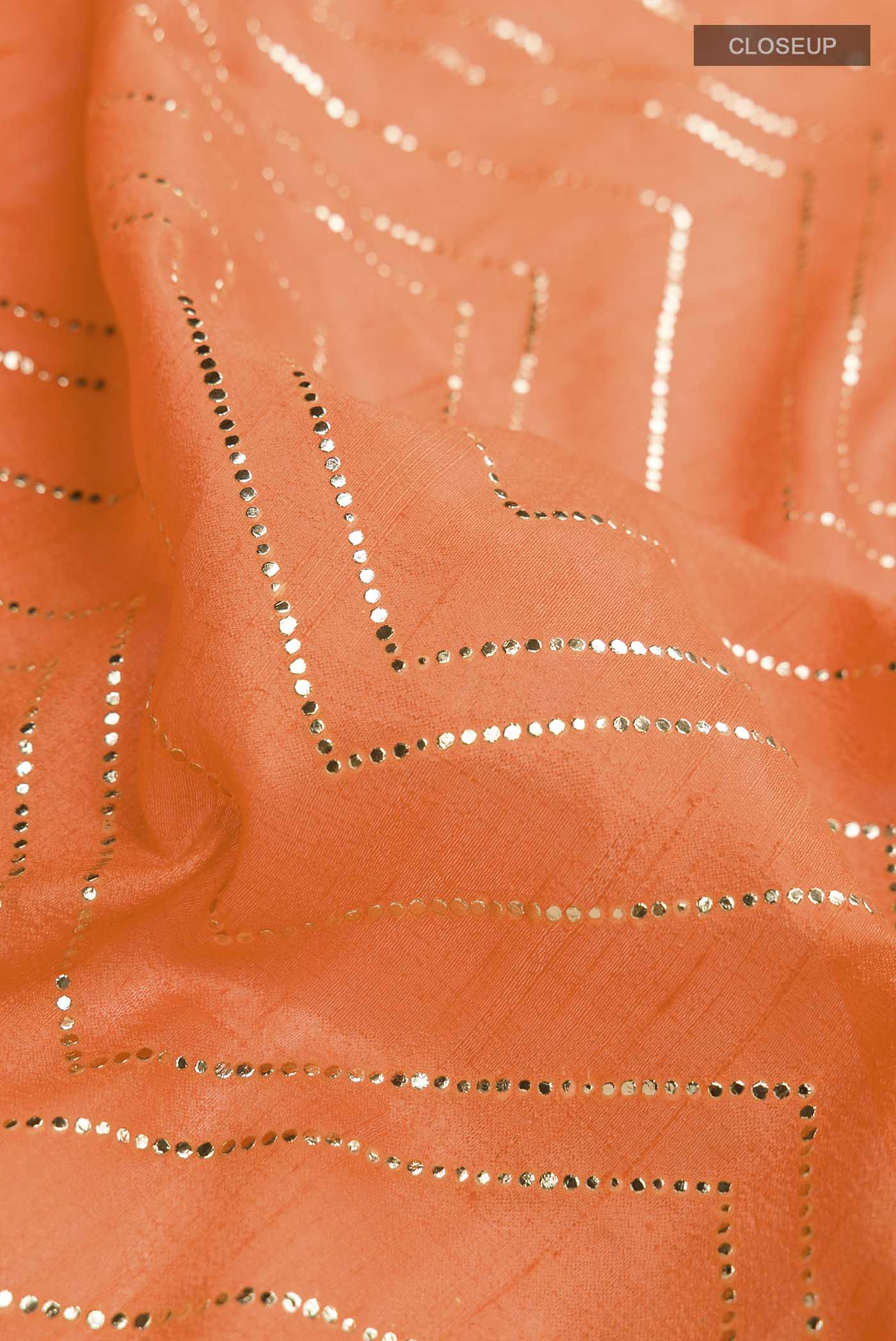 Close up of Orange Raw Silk Saree with Embroidery on the body and Zari Border displaying folds