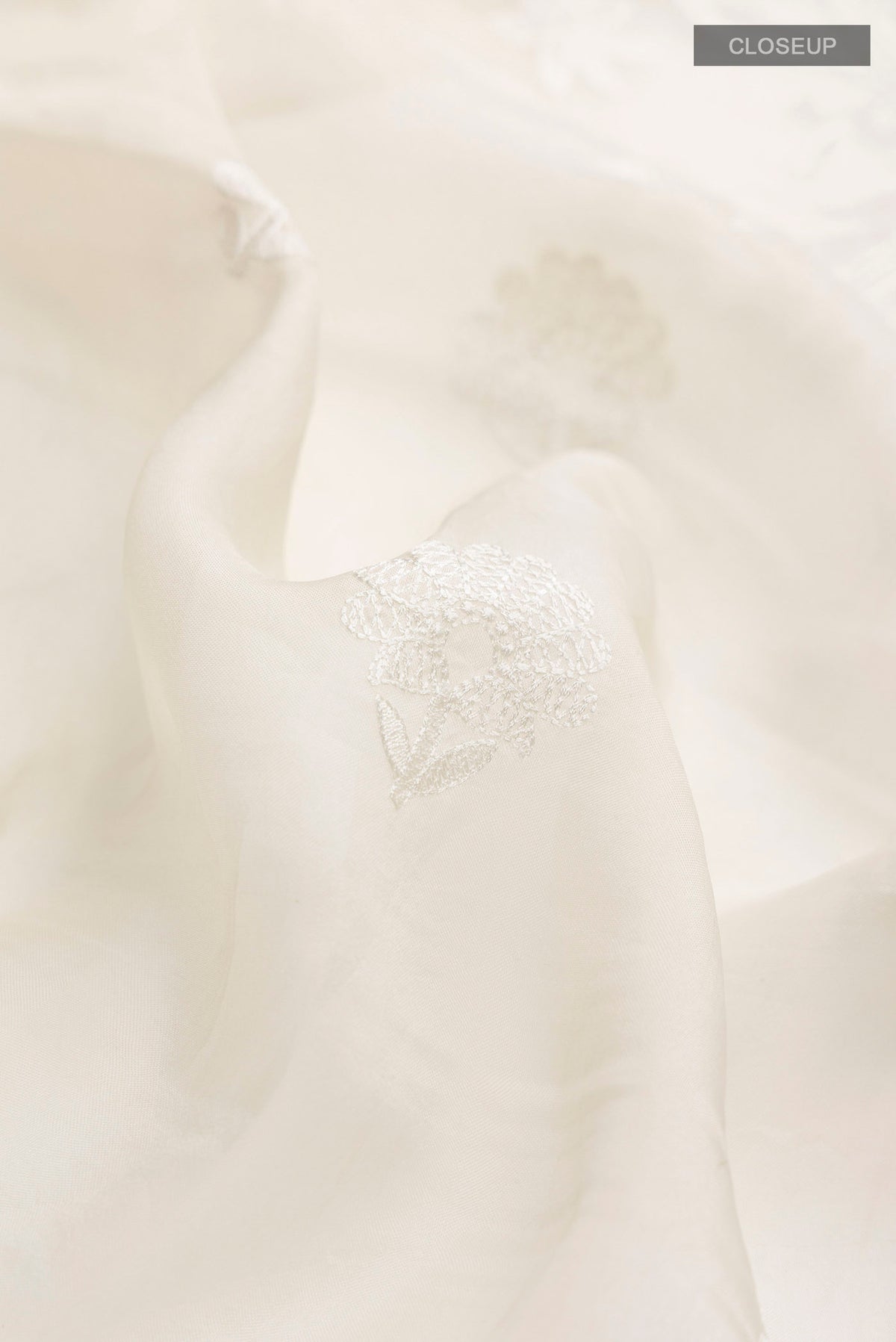 Close up of Off White Organza Silk Saree with Embroidery on the body and Embroidery Border displaying folds
