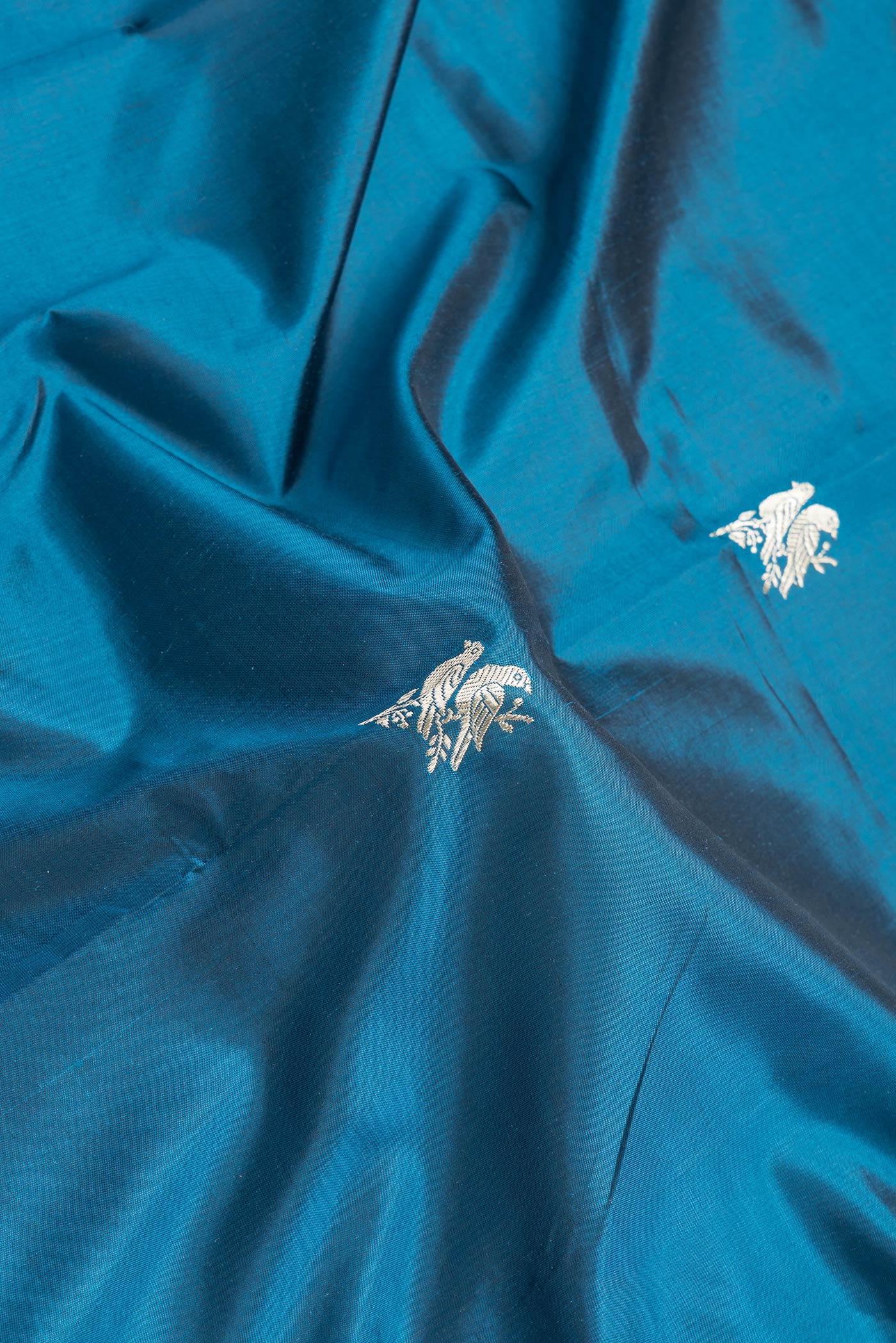 Close up of Peacock Blue Dual Tone Banarasi Silk Saree with Zari Butta on the body and Fancy Border.  displaying folds