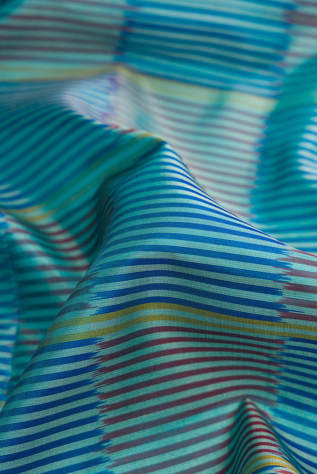 Close up of Peacock Blue Dual Tone Soft Silk Saree with Stripes on the body and Ikat Border.  displaying folds