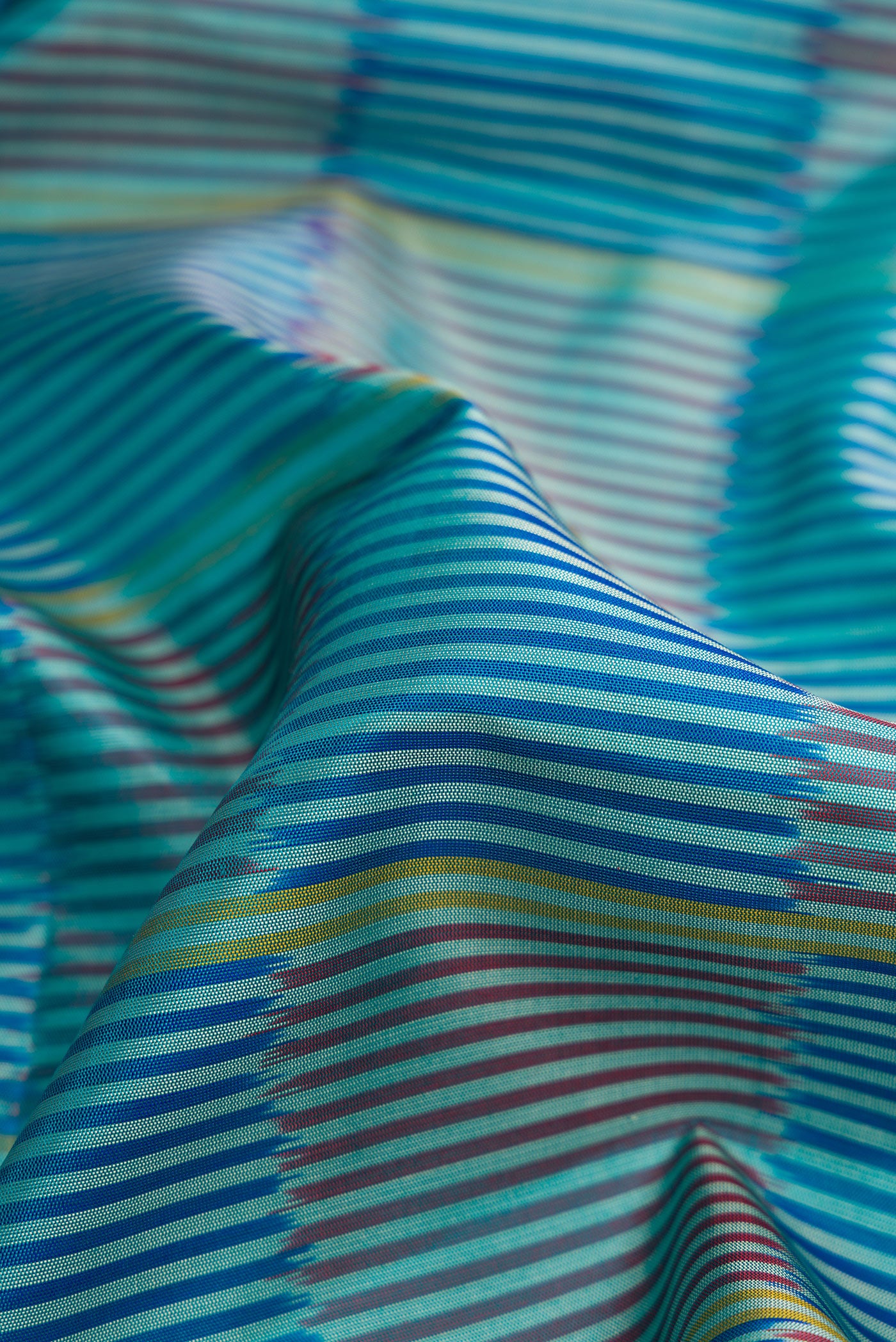 Close up of Peacock Blue Dual Tone Soft Silk Saree with Stripes on the body and Ikat Border.  displaying folds