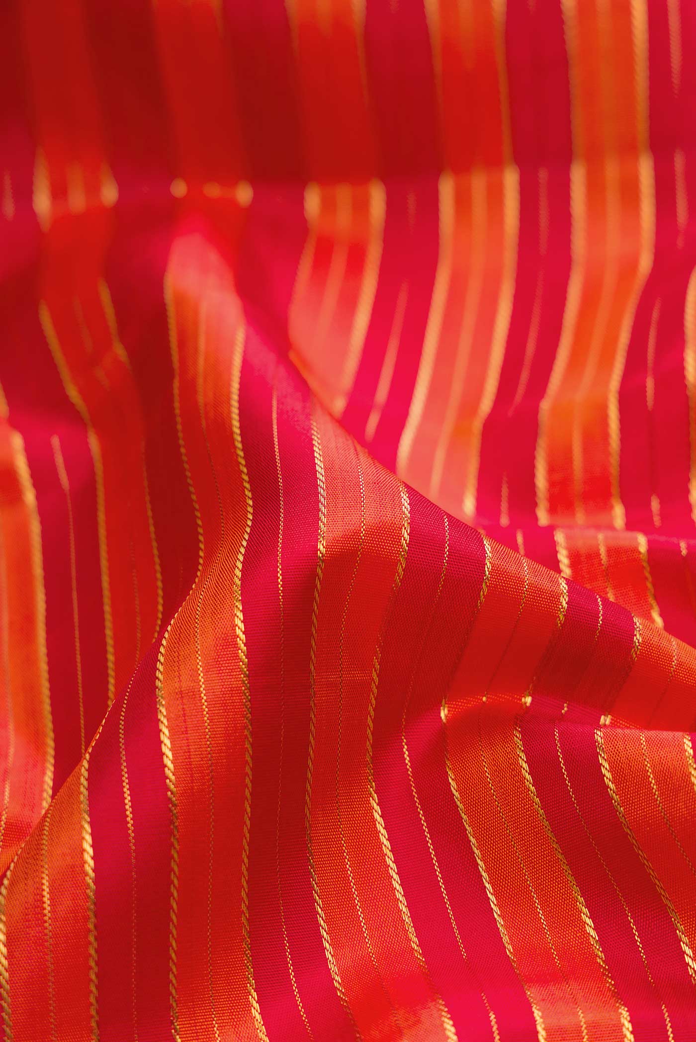 Close up of Pure Silk Pure Zari Orange Dual Tone Kanchipuram Saree with Stripes on the body and Zari Border displaying folds