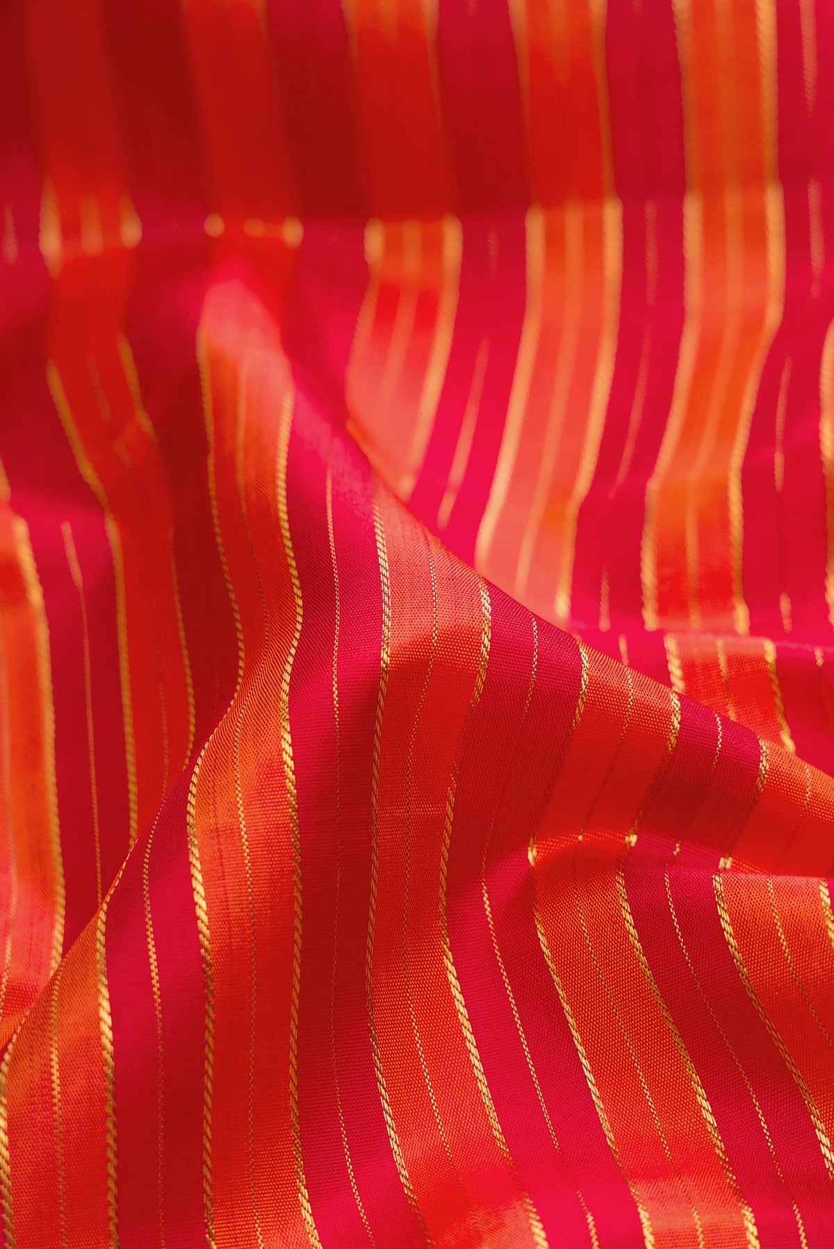 Close up of Pure Silk Pure Zari Orange Dual Tone Kanchipuram Saree with Stripes on the body and Zari Border displaying folds