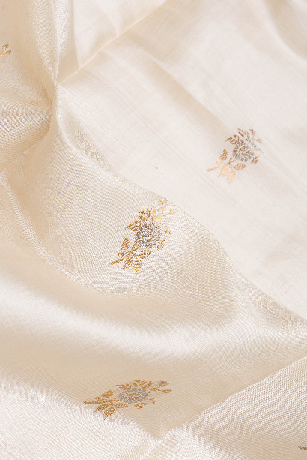 Close up of Beige Dual Tone Tussar Silk Saree with Zari Butta on the body and Zari Border.  displaying folds