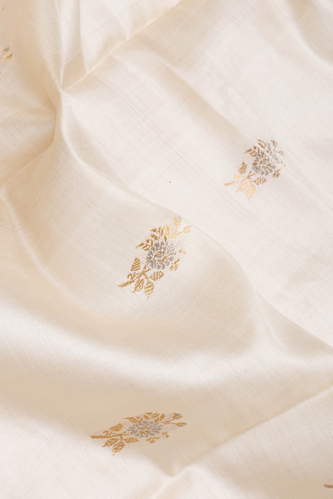 Close up of Beige Dual Tone Tussar Silk Saree with Zari Butta on the body and Zari Border.  displaying folds