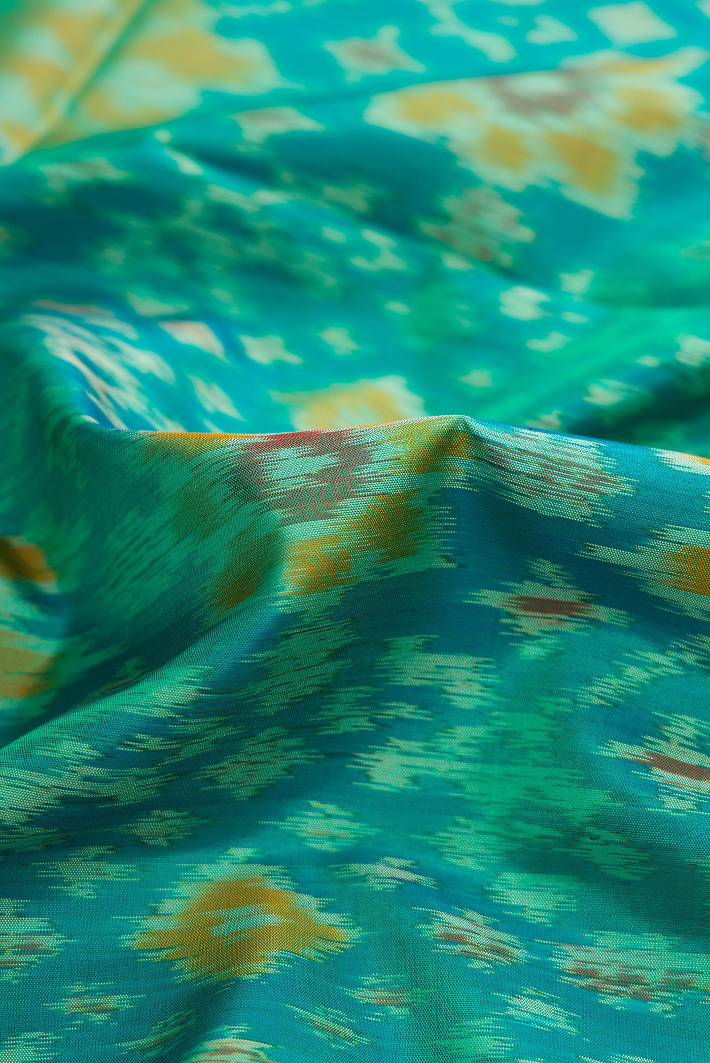 Close up of Sea Green Dual Tone Soft Silk Saree with Ikat Print on the body and Zari Border.  displaying folds