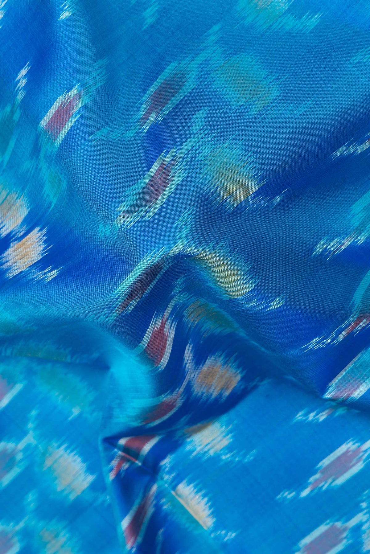 Close up of Pure Silk Peacock Blue Dual Tone Soft Saree with Ikat Print on the body and Zari Border.  displaying folds