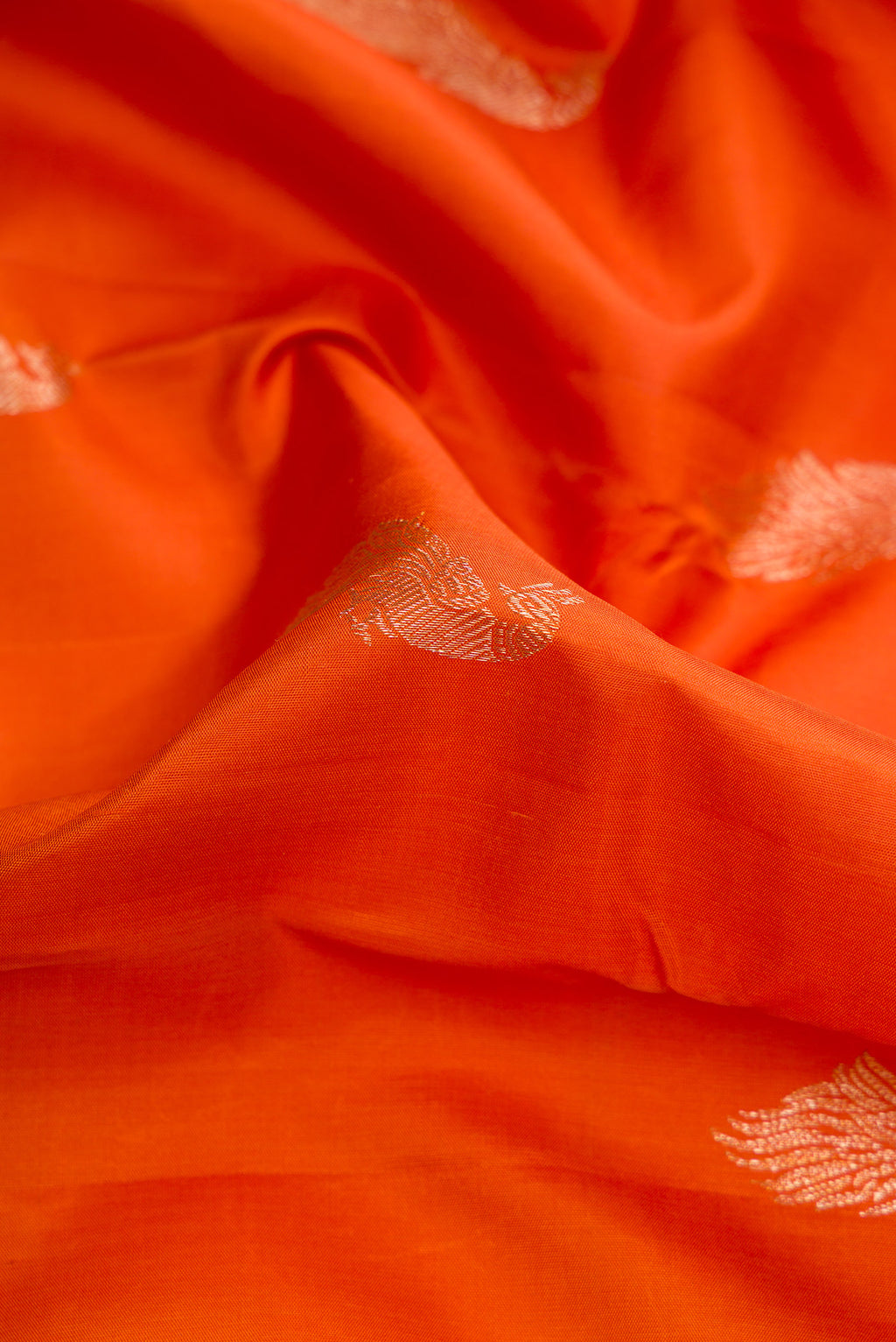 Close up of Pure Silk Pure Zari Brick Orange Dual Tone Kanjivaram Saree with Zari Butta on the body and Zari Border.  displaying folds
