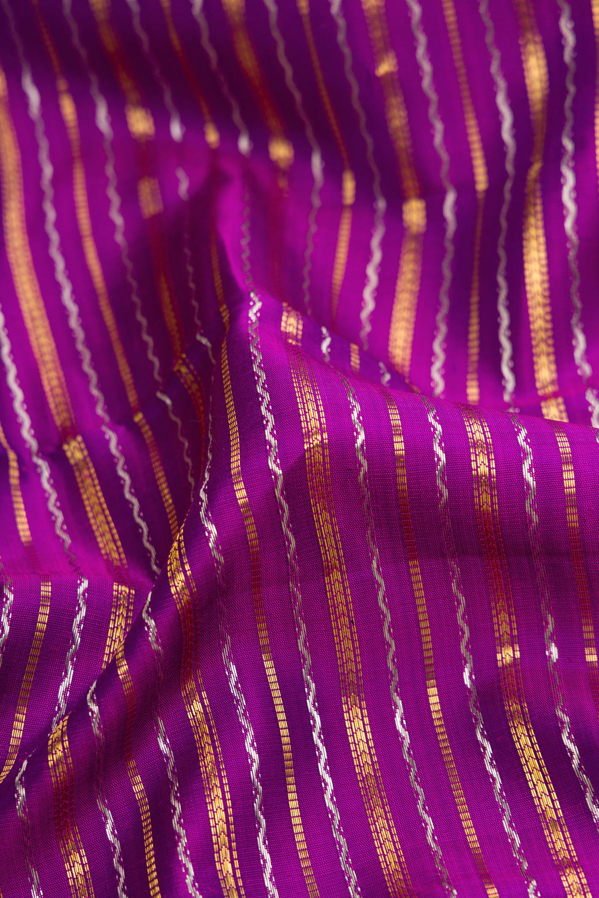 Close up of Magenta Dual Tone Kanchipuram Silk Saree with Stripes on the body and Zari Border.  displaying folds